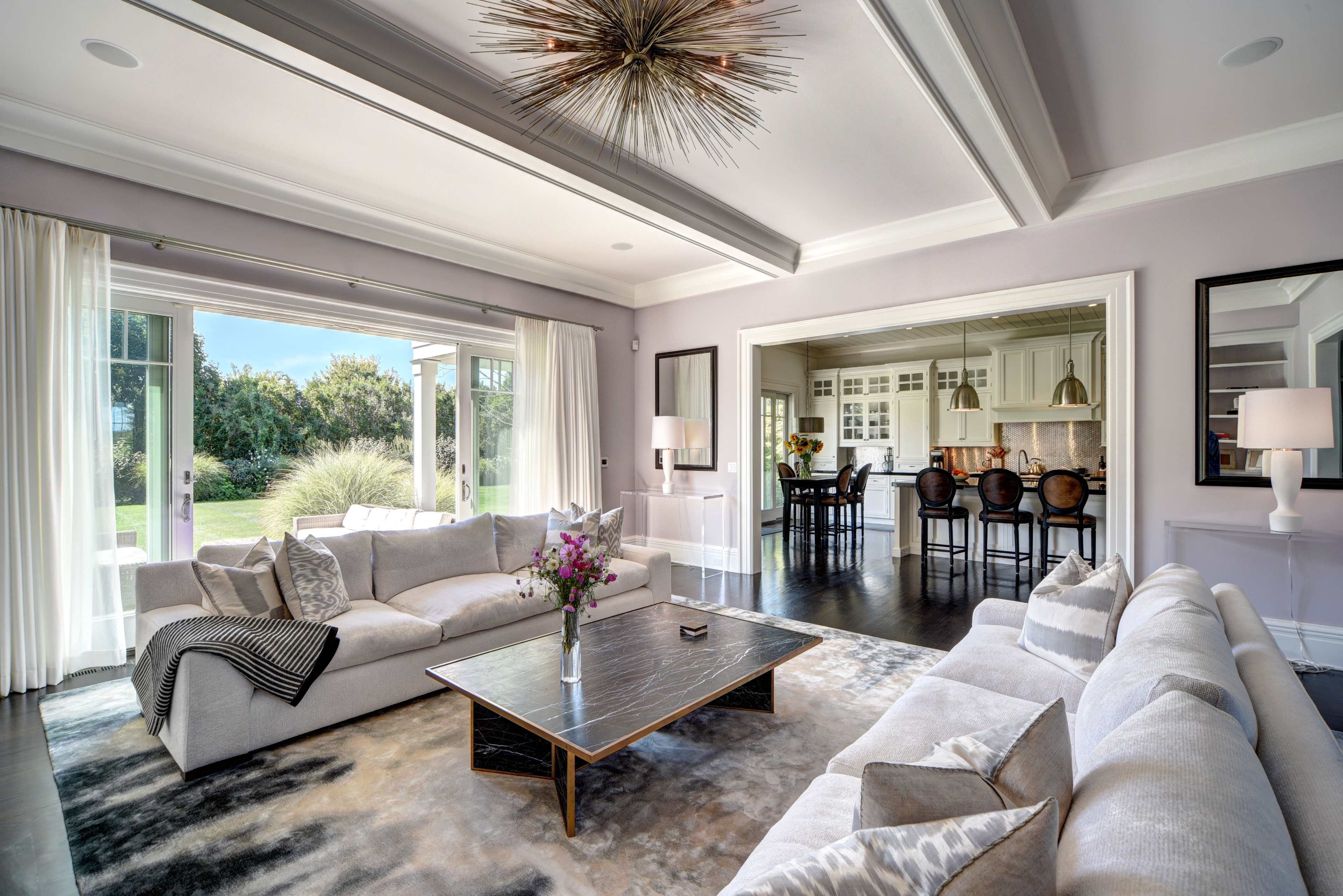 The living room features a modern design with a large sectional sofa, a central coffee table, and an open view of a kitchen area.