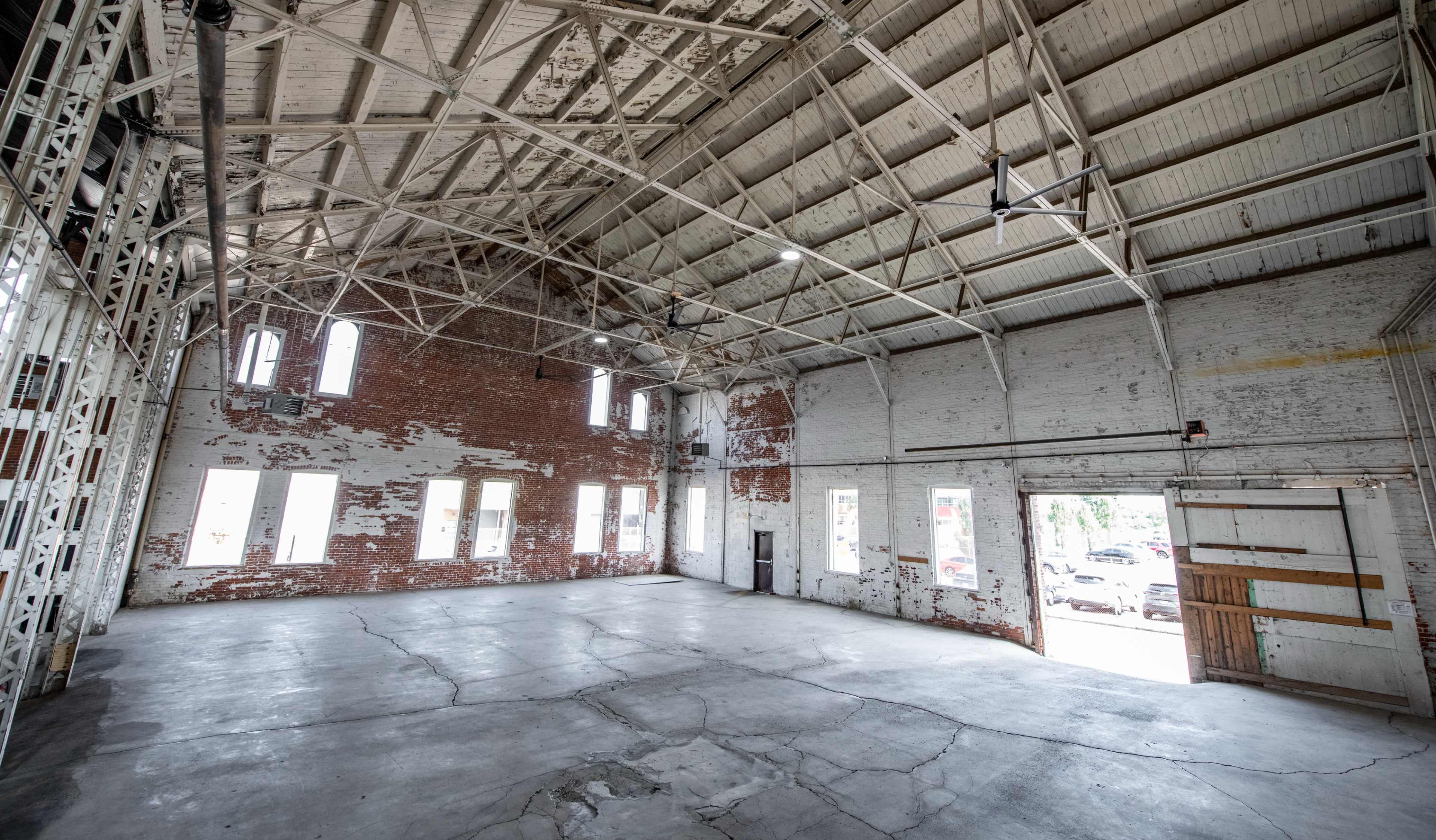 A spacious, empty industrial warehouse with exposed brick walls and a high ceiling.