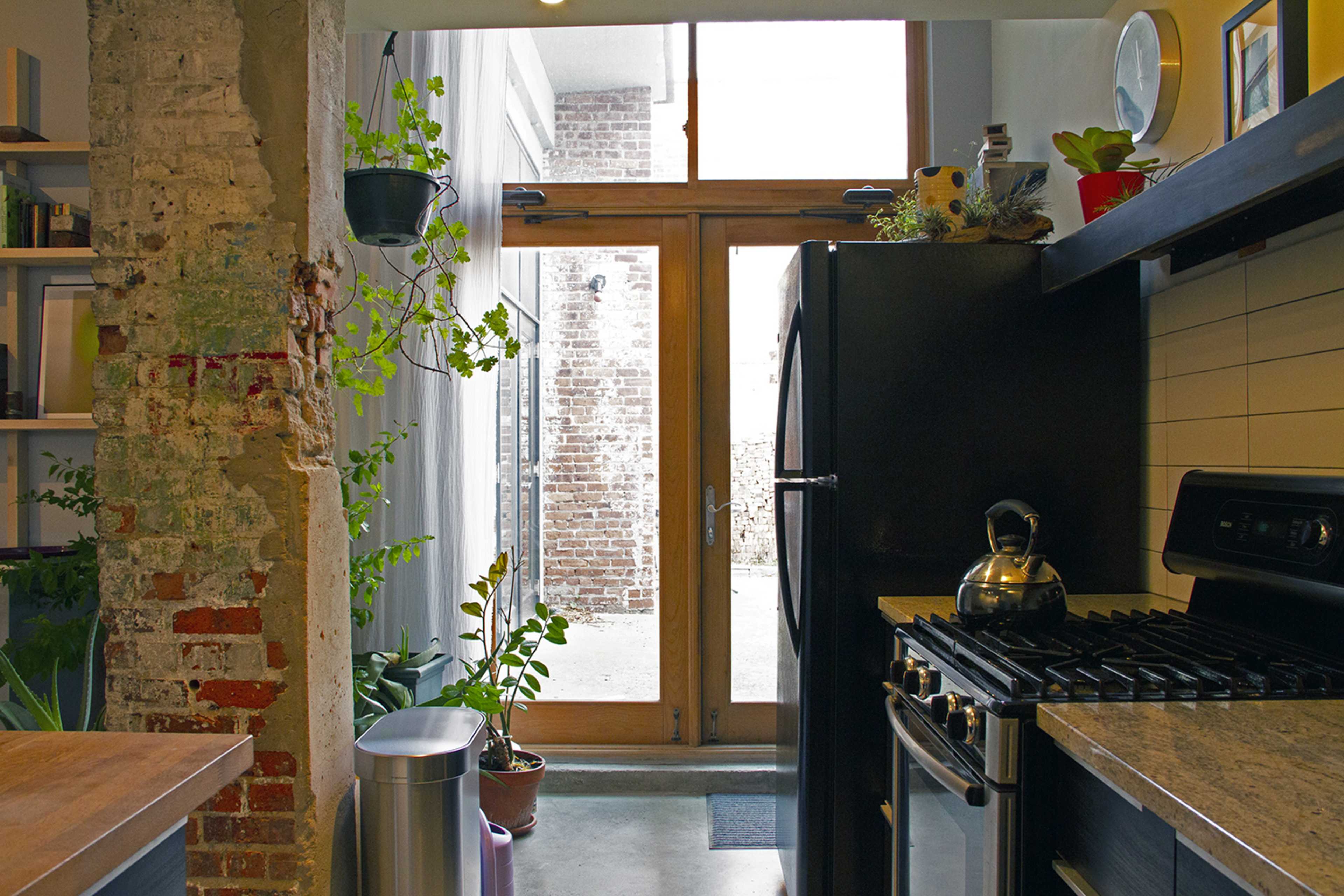 A modern kitchen with a view of an interior courtyard through large glass doors framed by exposed brick and plants.