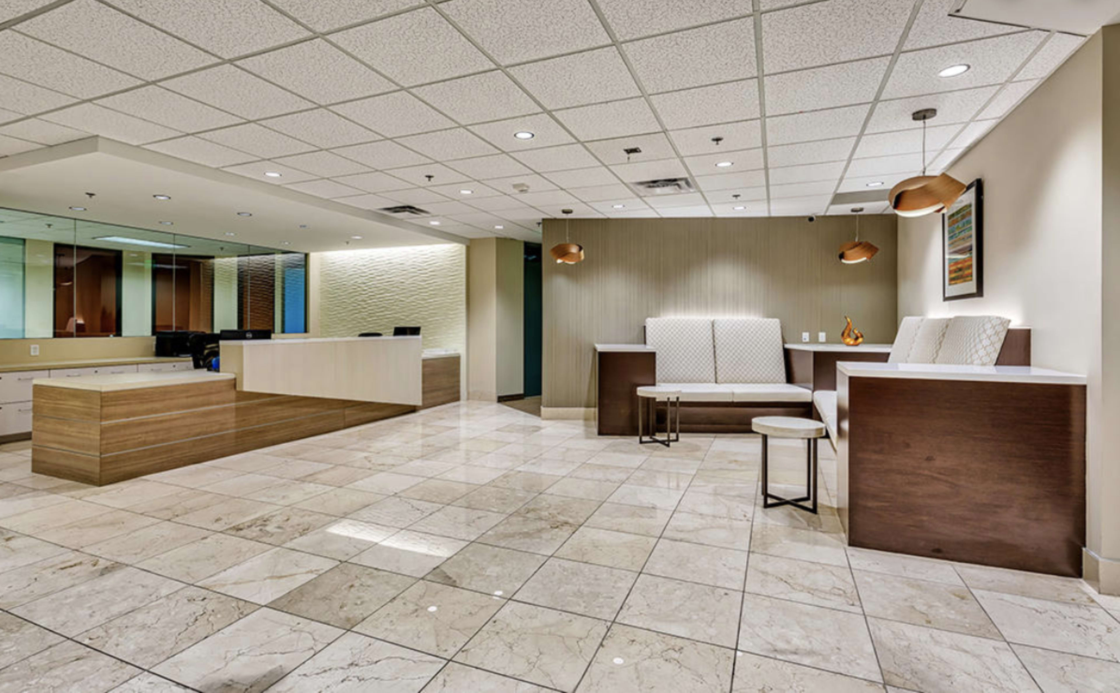 A modern reception area with tiled flooring, a large front desk, and seating arrangements against the walls.