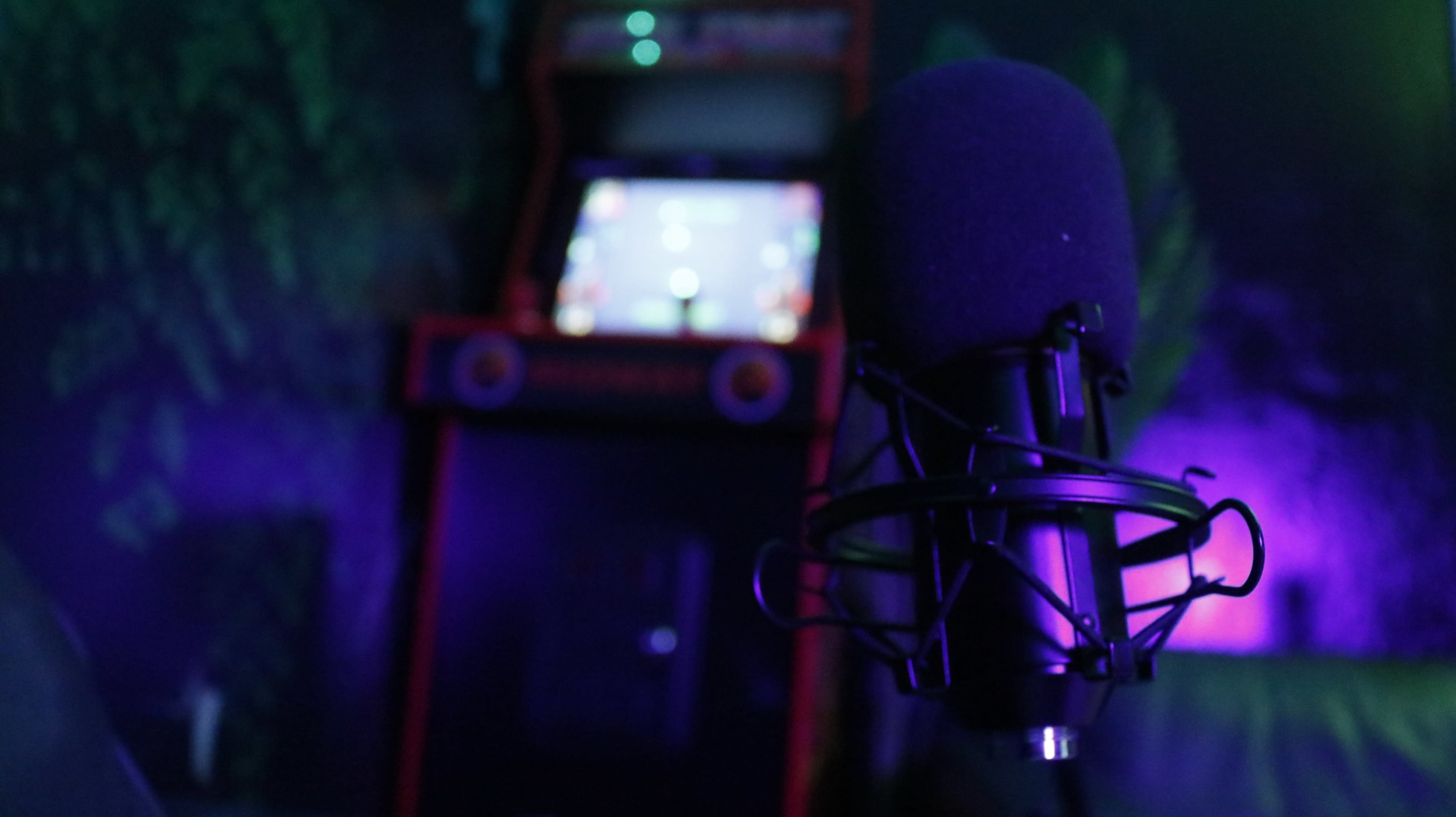 A black microphone is prominently placed in the foreground with a retro arcade machine glowing in the background.