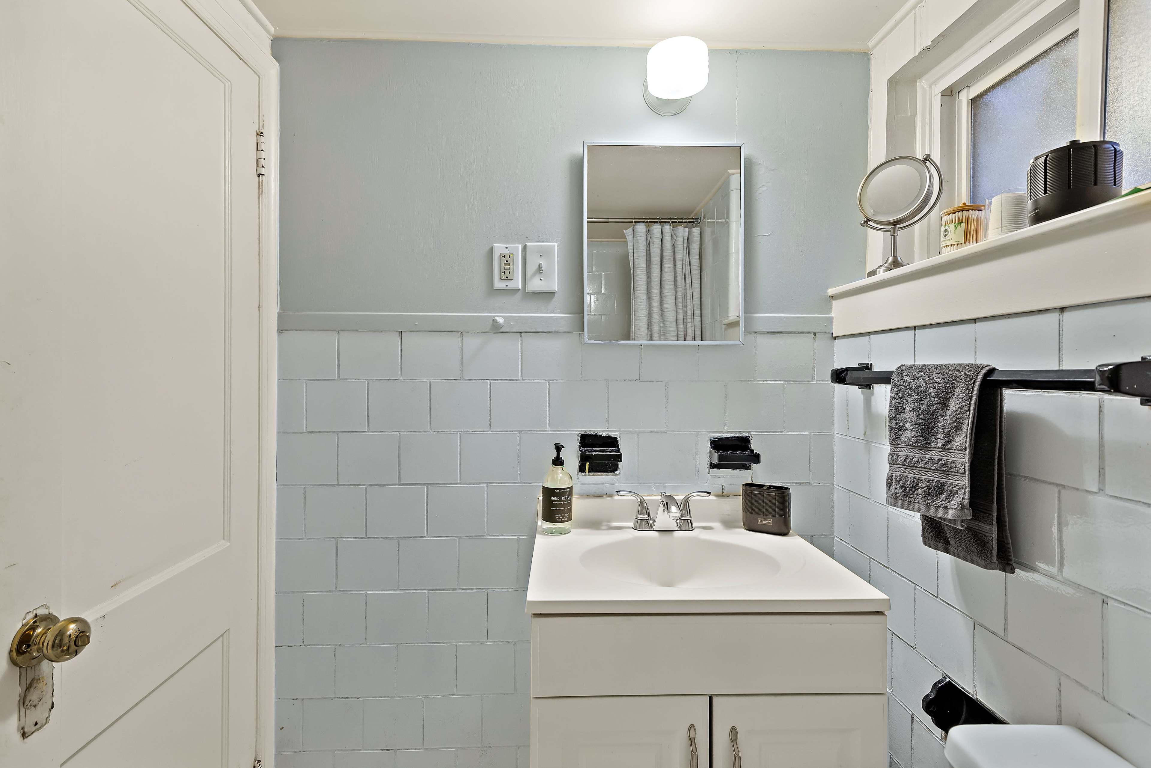A small bathroom with a white vanity, a mirror, and blue tiled walls.