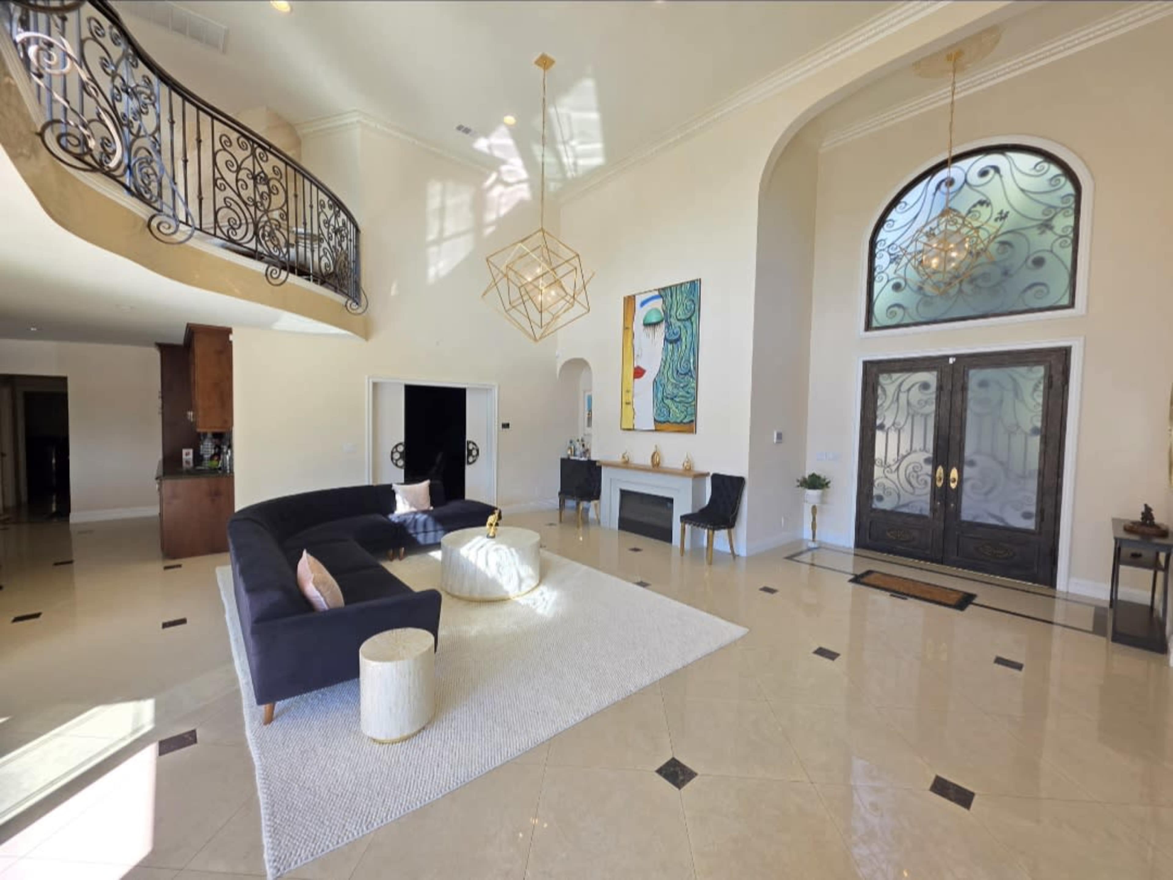 A spacious living room features a black sofa, a white rug, and large arched windows with decorative lighting.