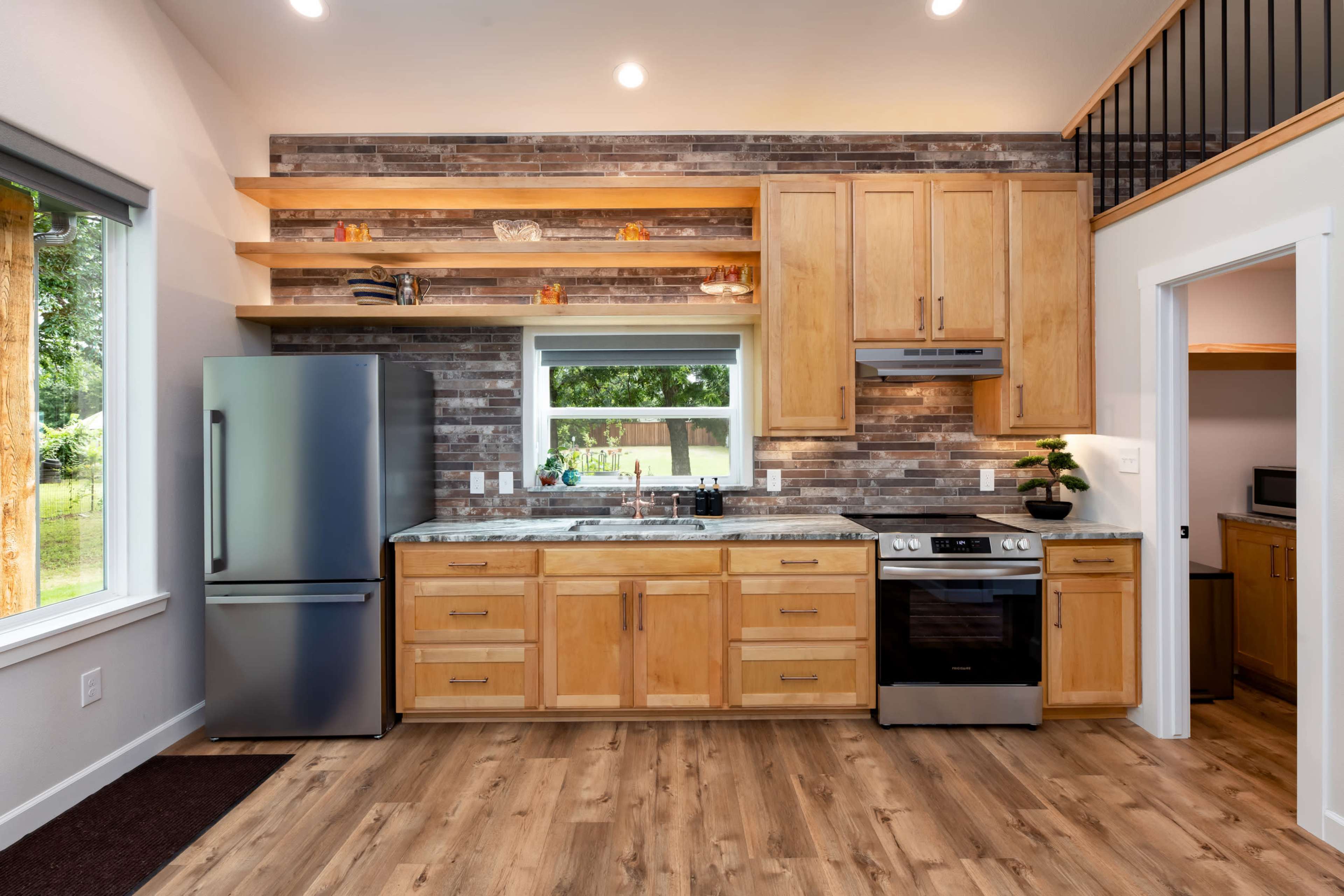 The image shows a modern kitchen with wooden cabinets, stainless steel appliances, and a stone backsplash.
