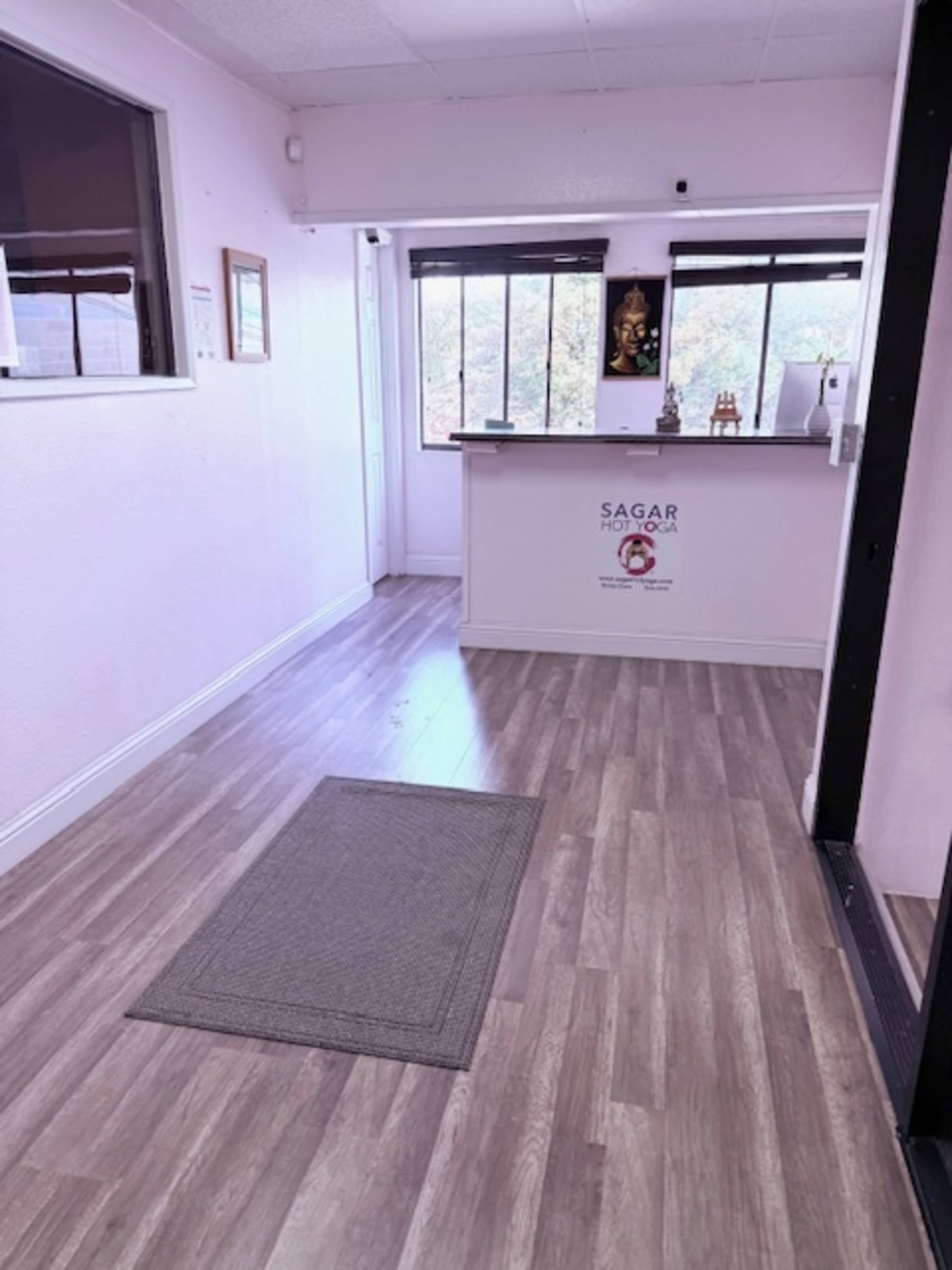 The image shows a light-colored reception area with a gray mat on the floor and a counter adorned with a decorative piece in the background.