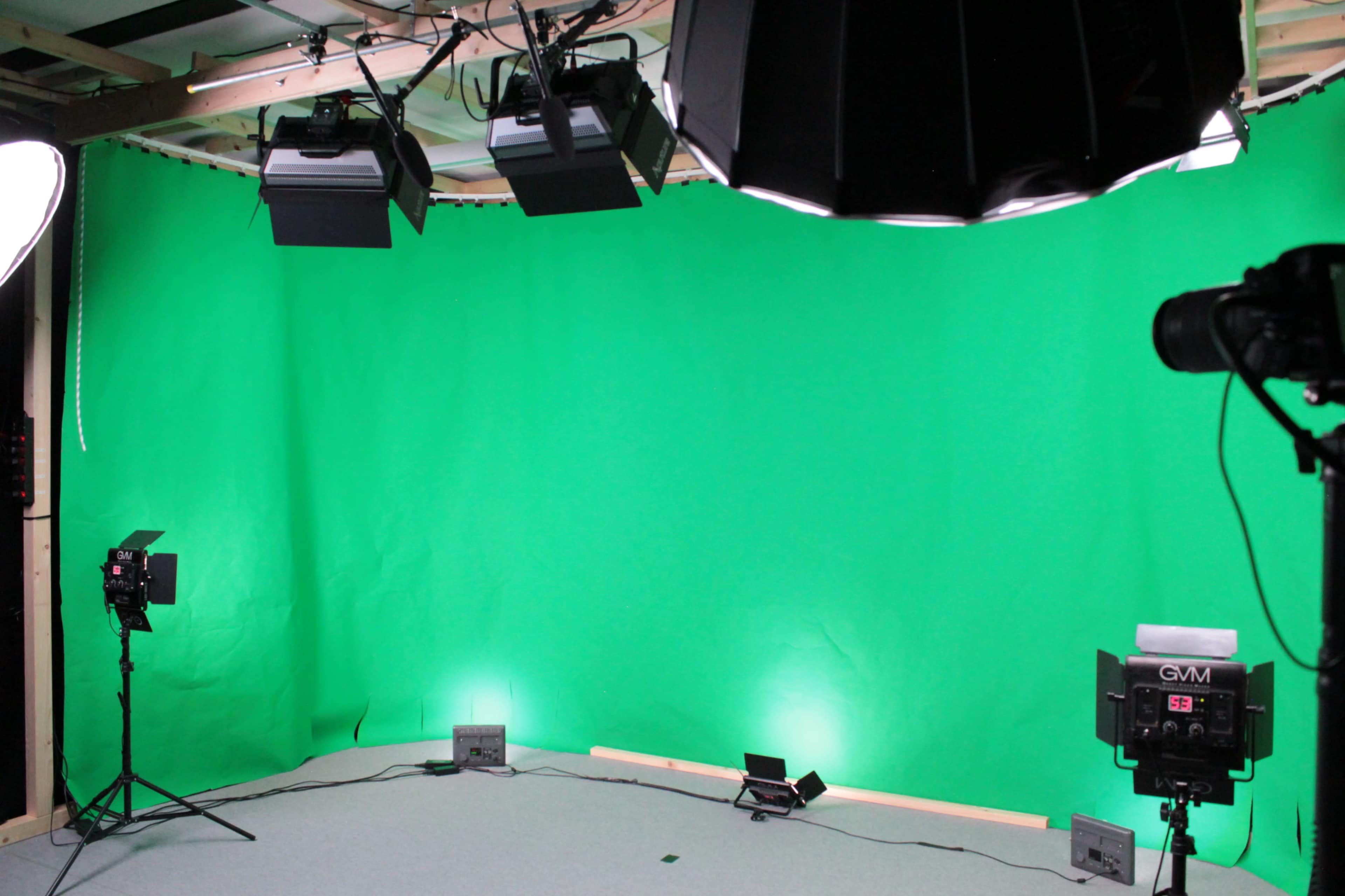The image shows a green screen studio setup with various lighting equipment and cameras positioned around the space.