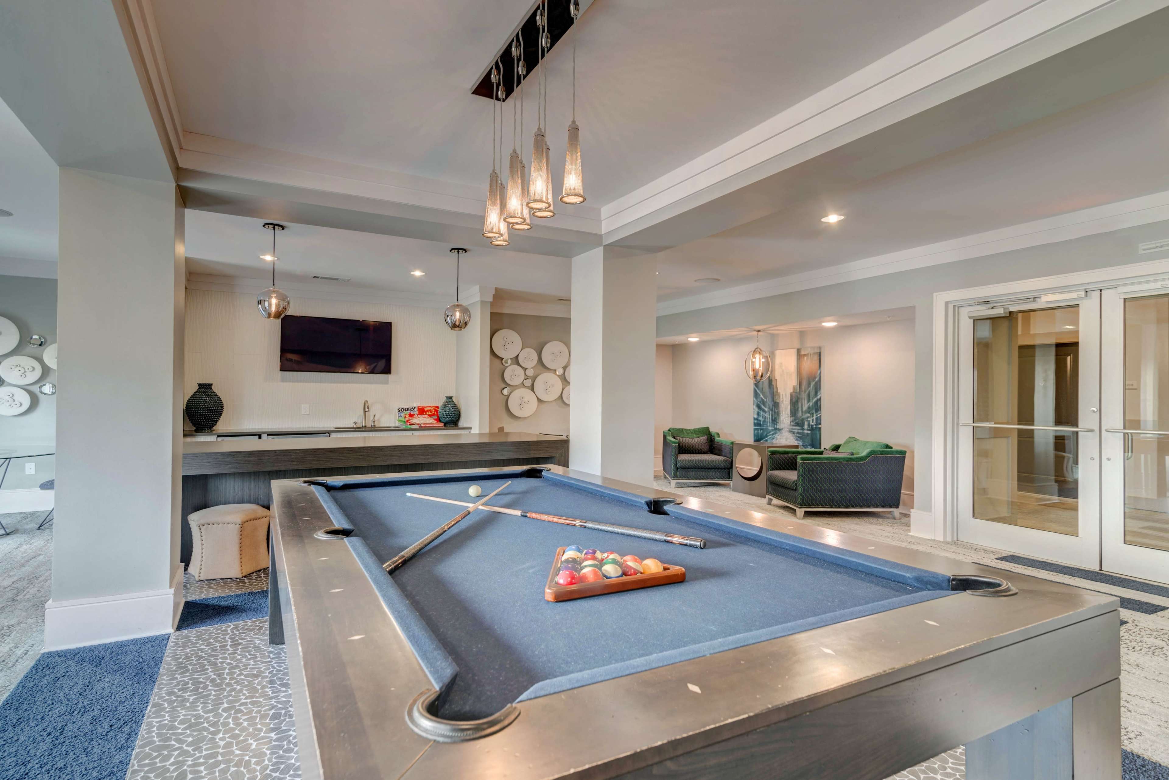 A pool table with a triangular rack of balls is positioned in a well-lit recreational room featuring a seating area and wall decorations.