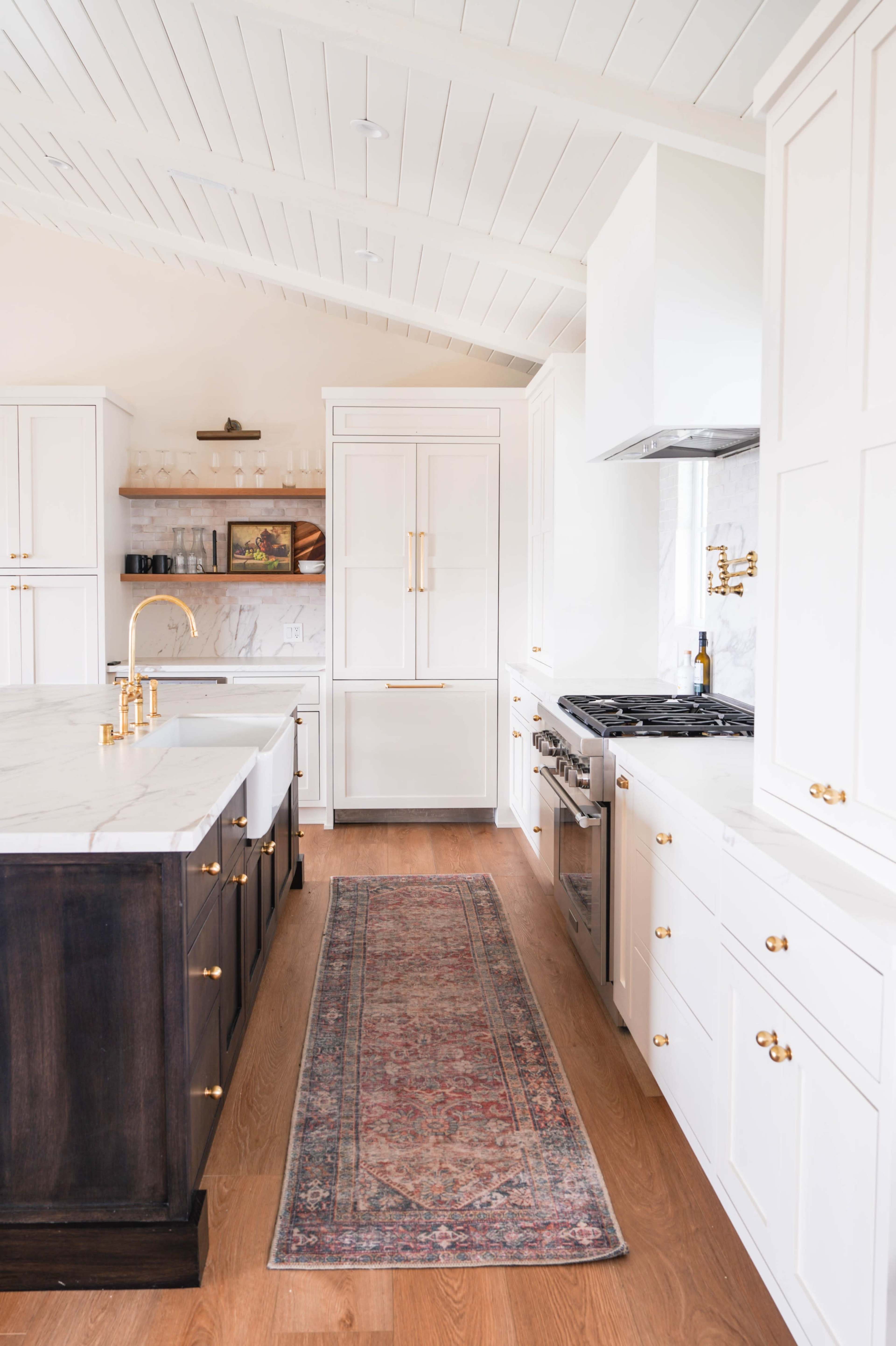 The kitchen features white cabinetry, a marble island with a sink, and a wooden floor with a vintage rug running through the center.
