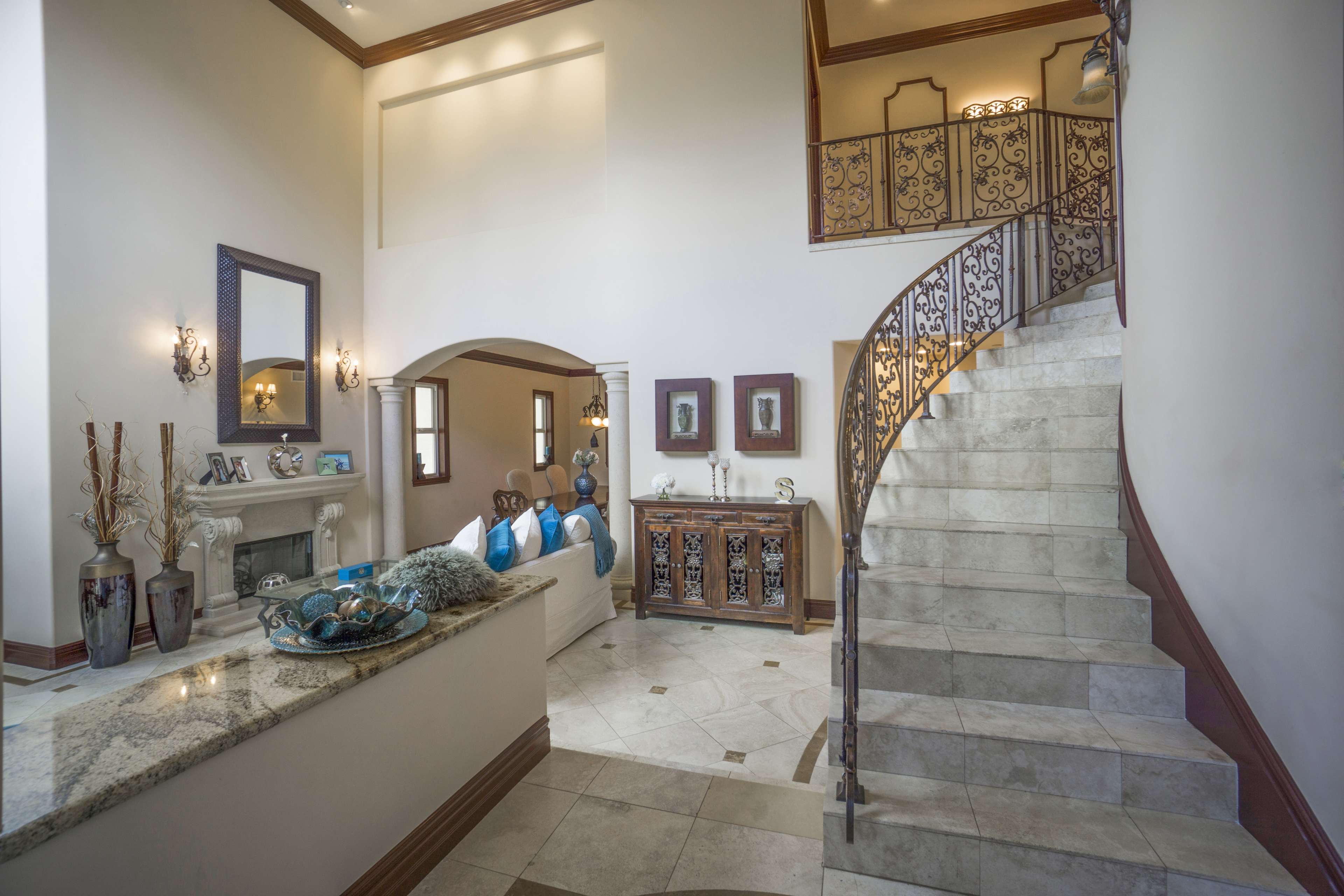 A spacious entryway features a curved staircase, a granite countertop, and decorative furnishings against neutral walls.