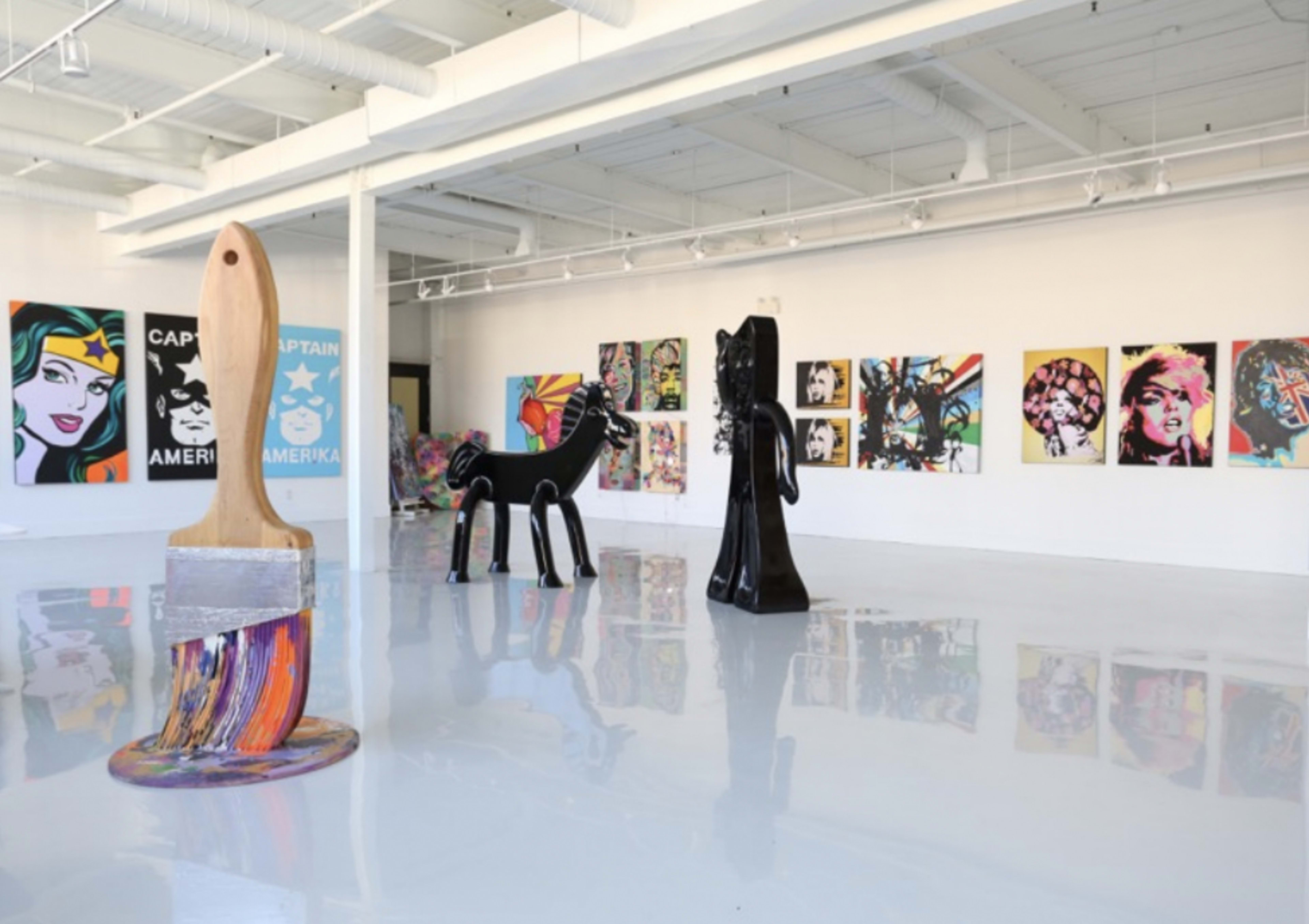 An art gallery featuring colorful paintings on the walls and large sculptural pieces, including a paintbrush and a horse.