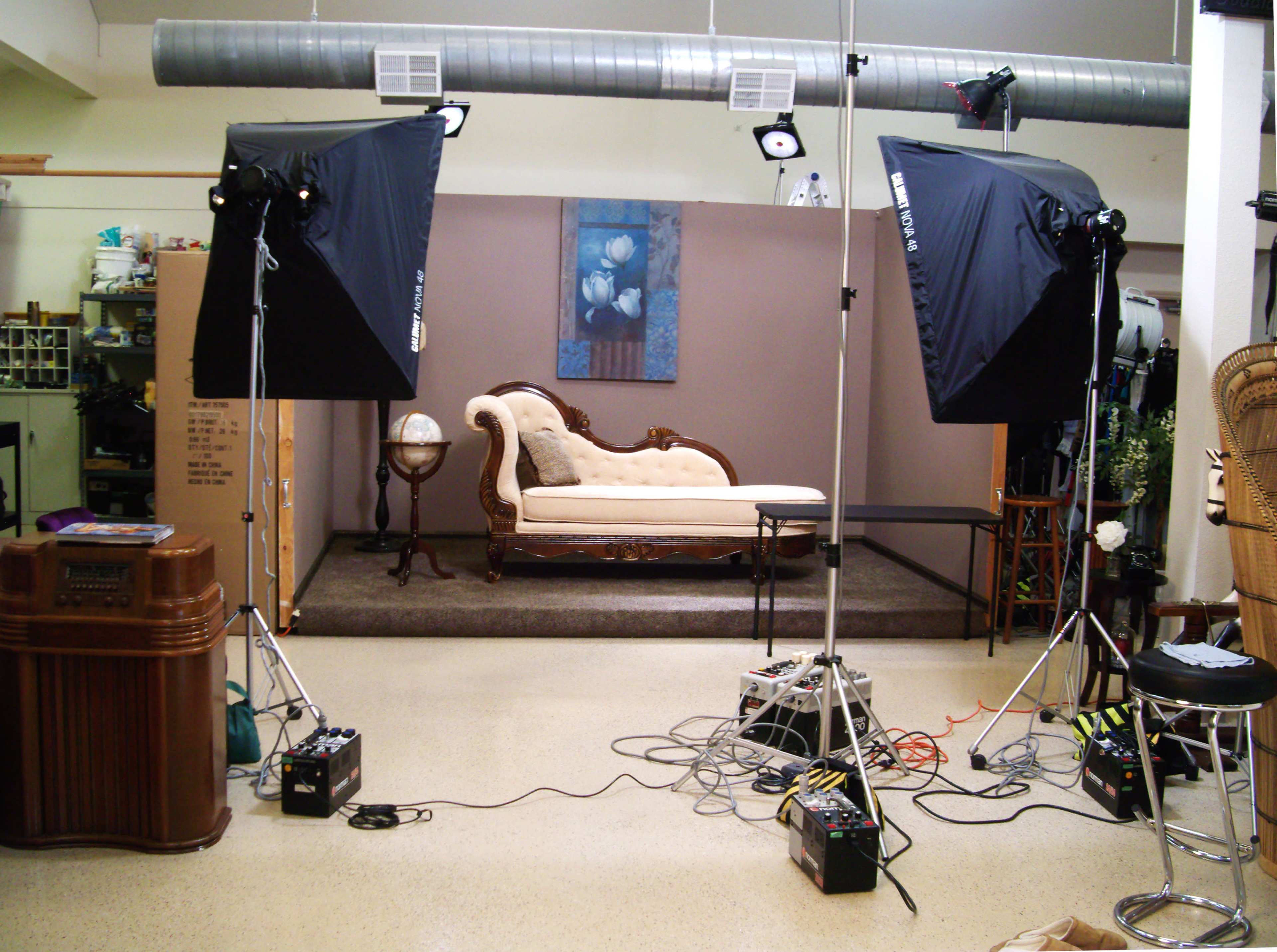 A photography studio set up with two large softbox lights, a vintage sofa, and various electrical equipment on the floor.