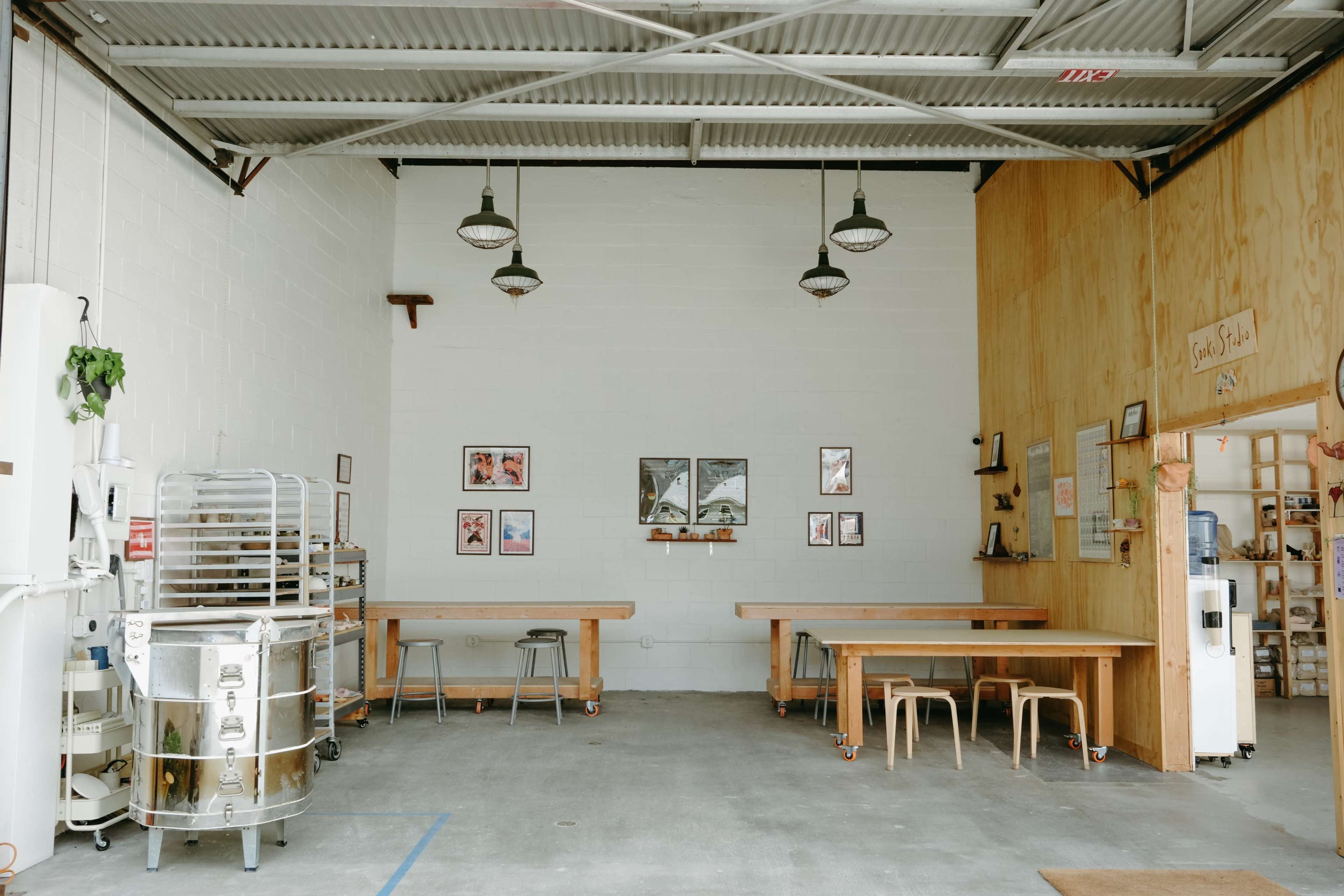 A spacious, industrial-style interior with wooden tables, metal stools, and framed pictures on the walls, illuminated by pendant lights.