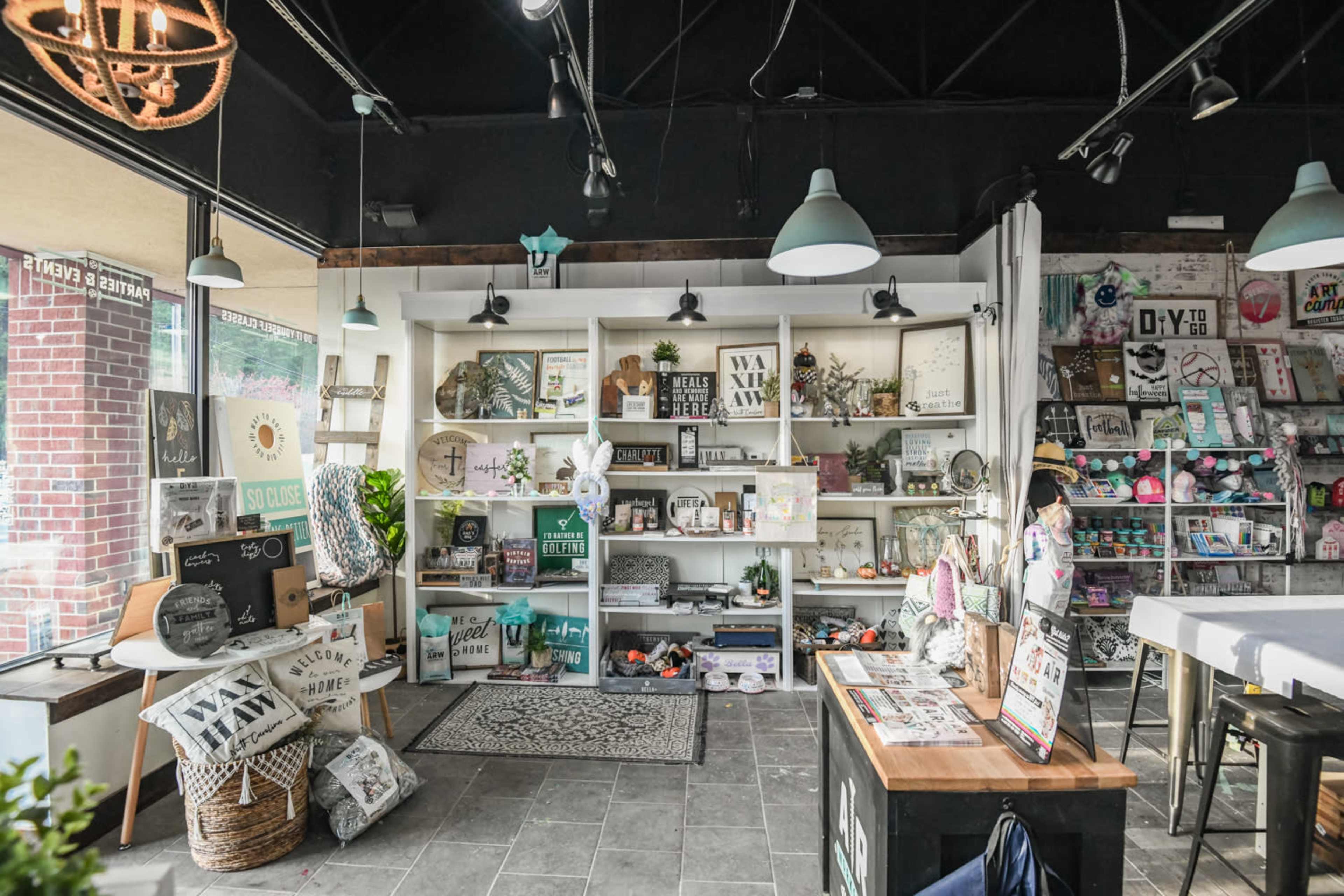 A boutique interior featuring shelves filled with various home decor items, crafts, and accessories, with a seating area and large windows.