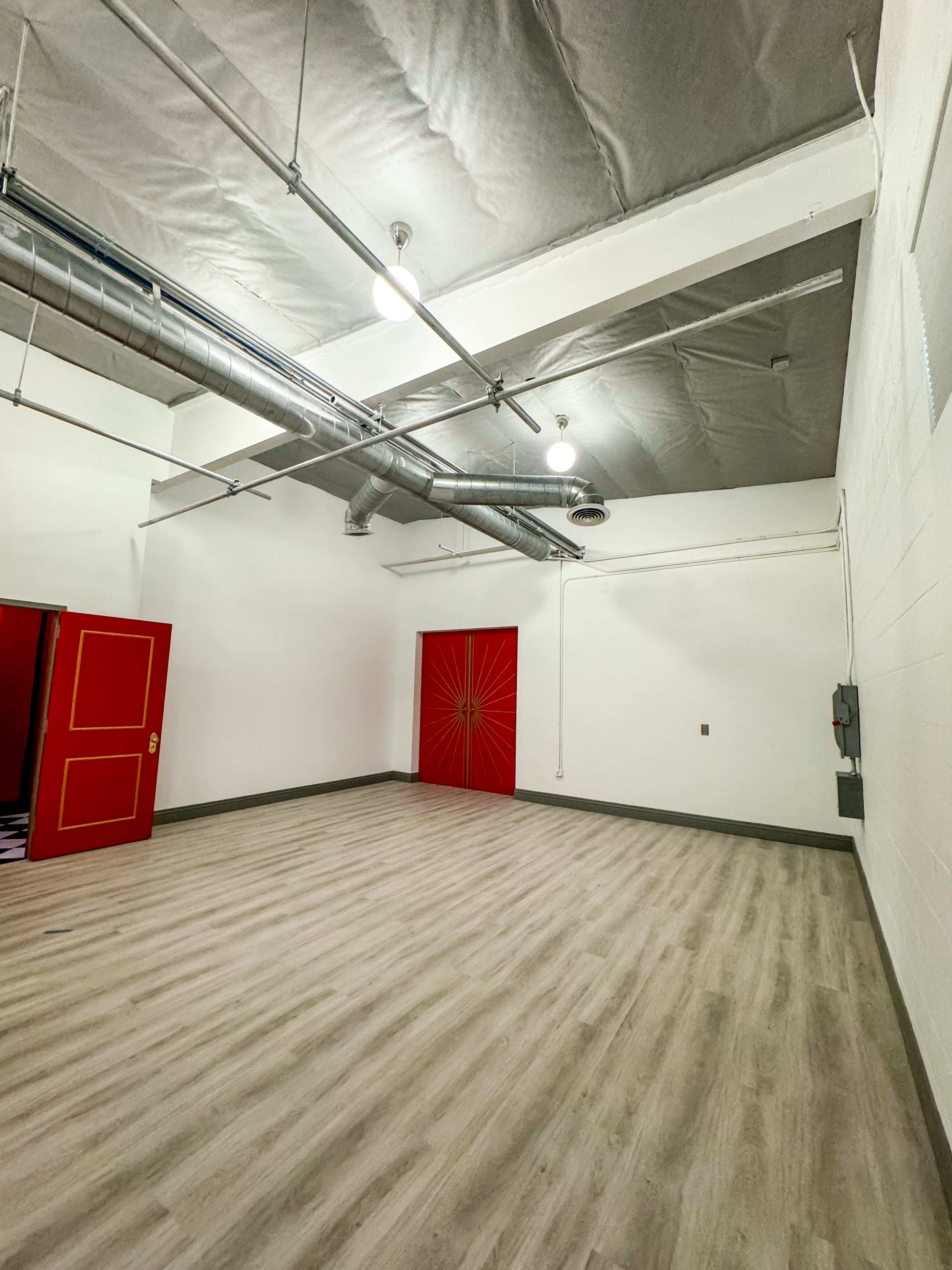 An empty room with gray walls, a light-colored wooden floor, and a red door featuring a sunburst design.