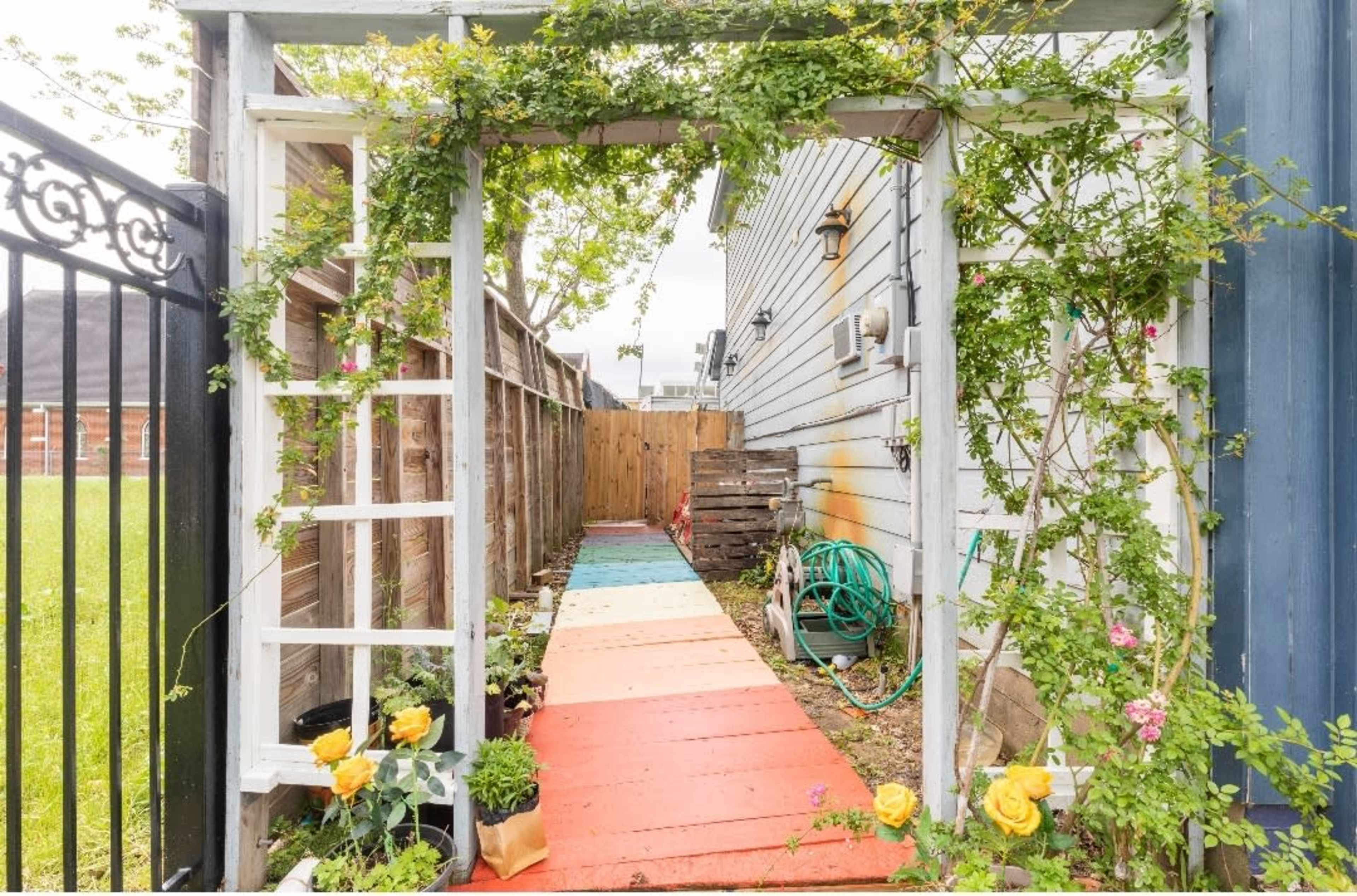 A colorful path leads through an archway adorned with greenery alongside a wooden fence.