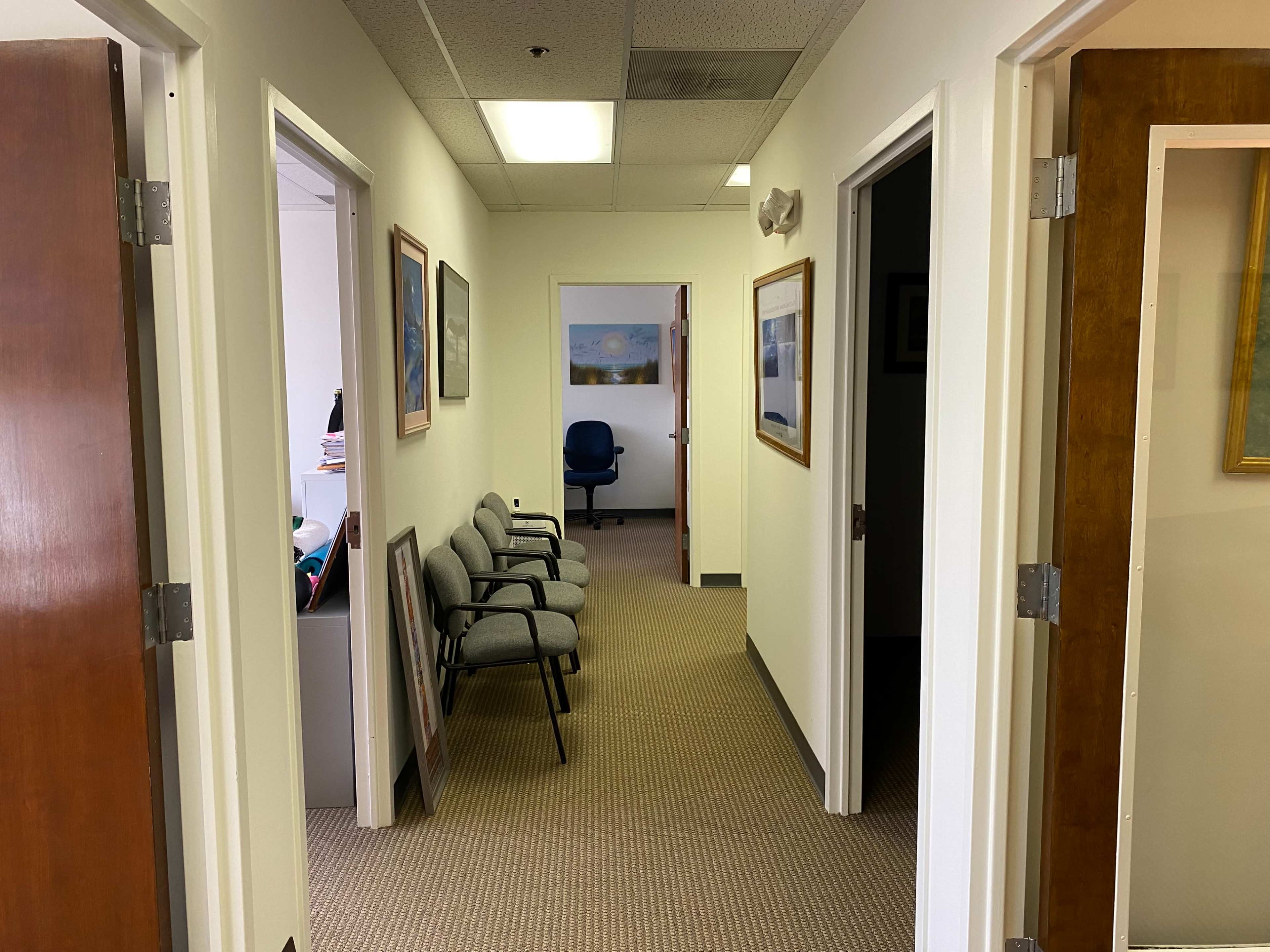 A hallway leads to several office doors, with chairs positioned against one wall and a desk visible in the background.