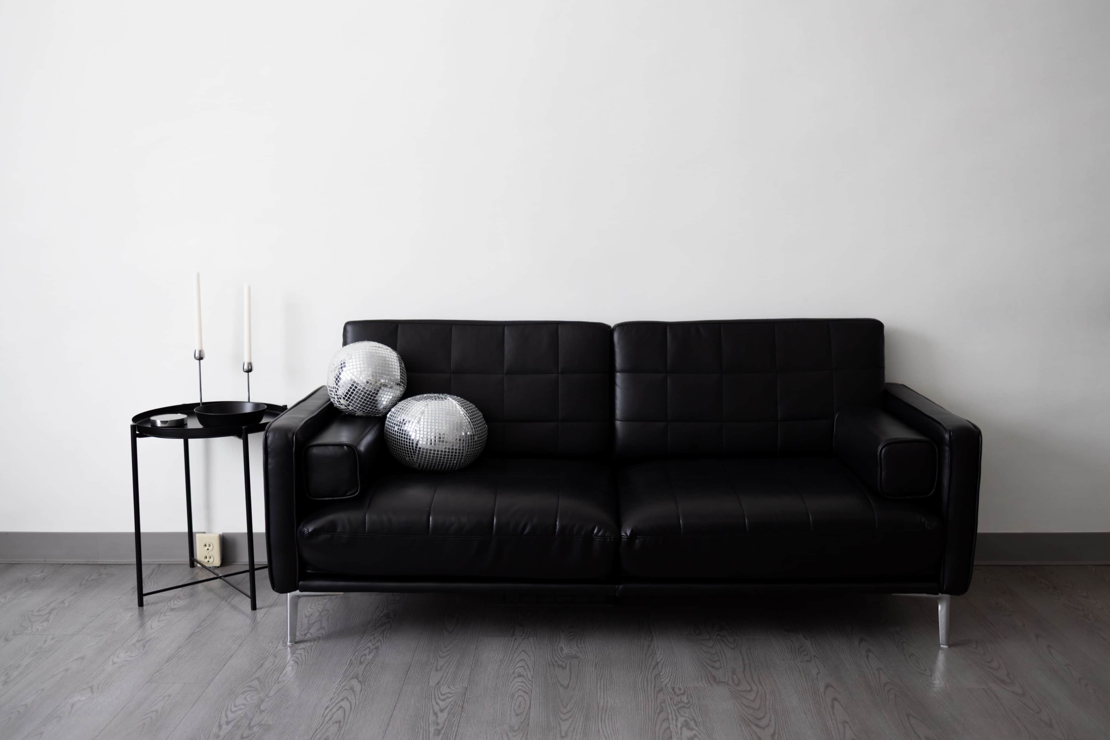 A black leather sofa with two disco balls on the seat sits next to a small, round table with two candles.