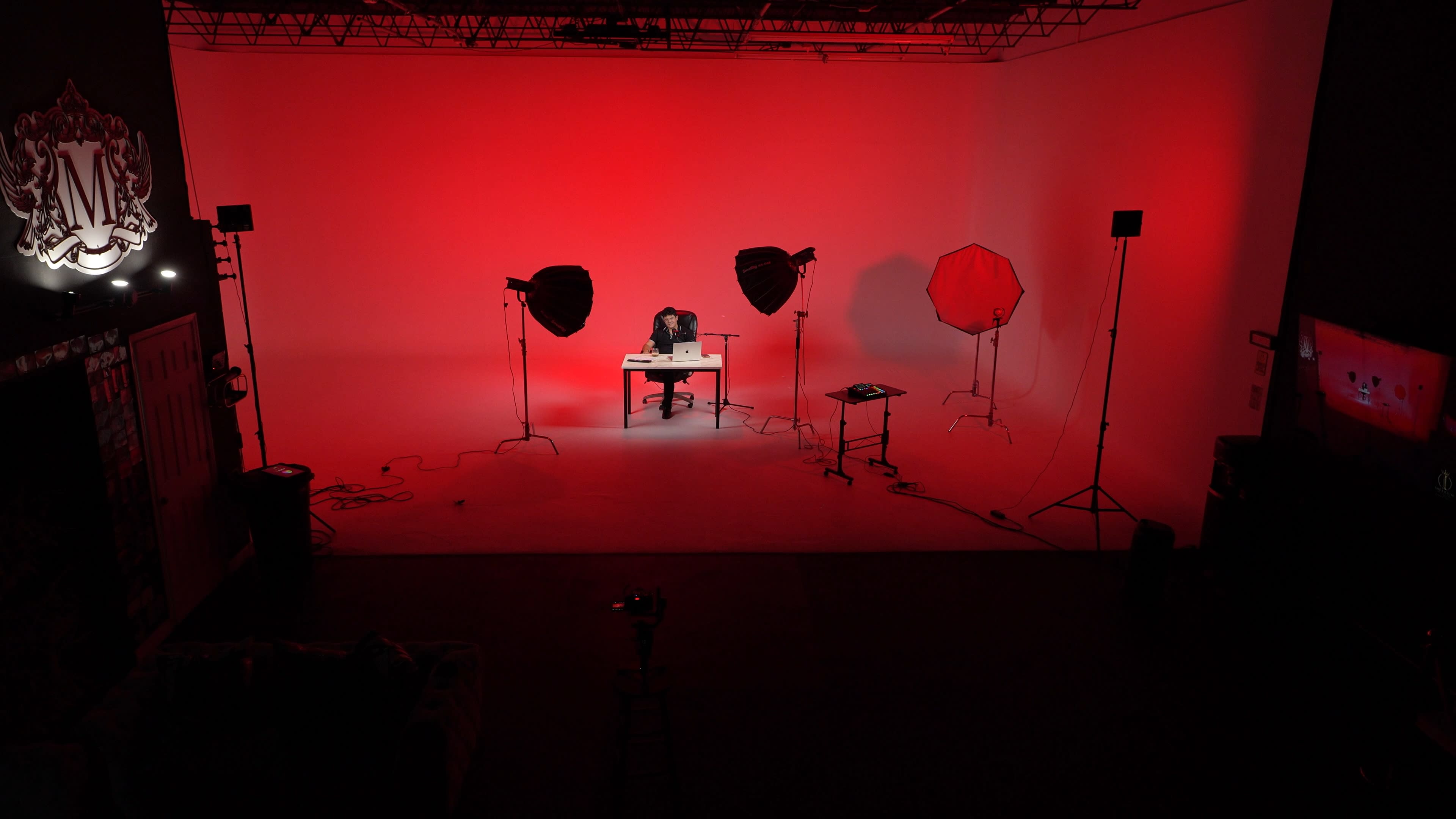 A person is sitting at a desk under bright studio lights in a red-lit photo studio.