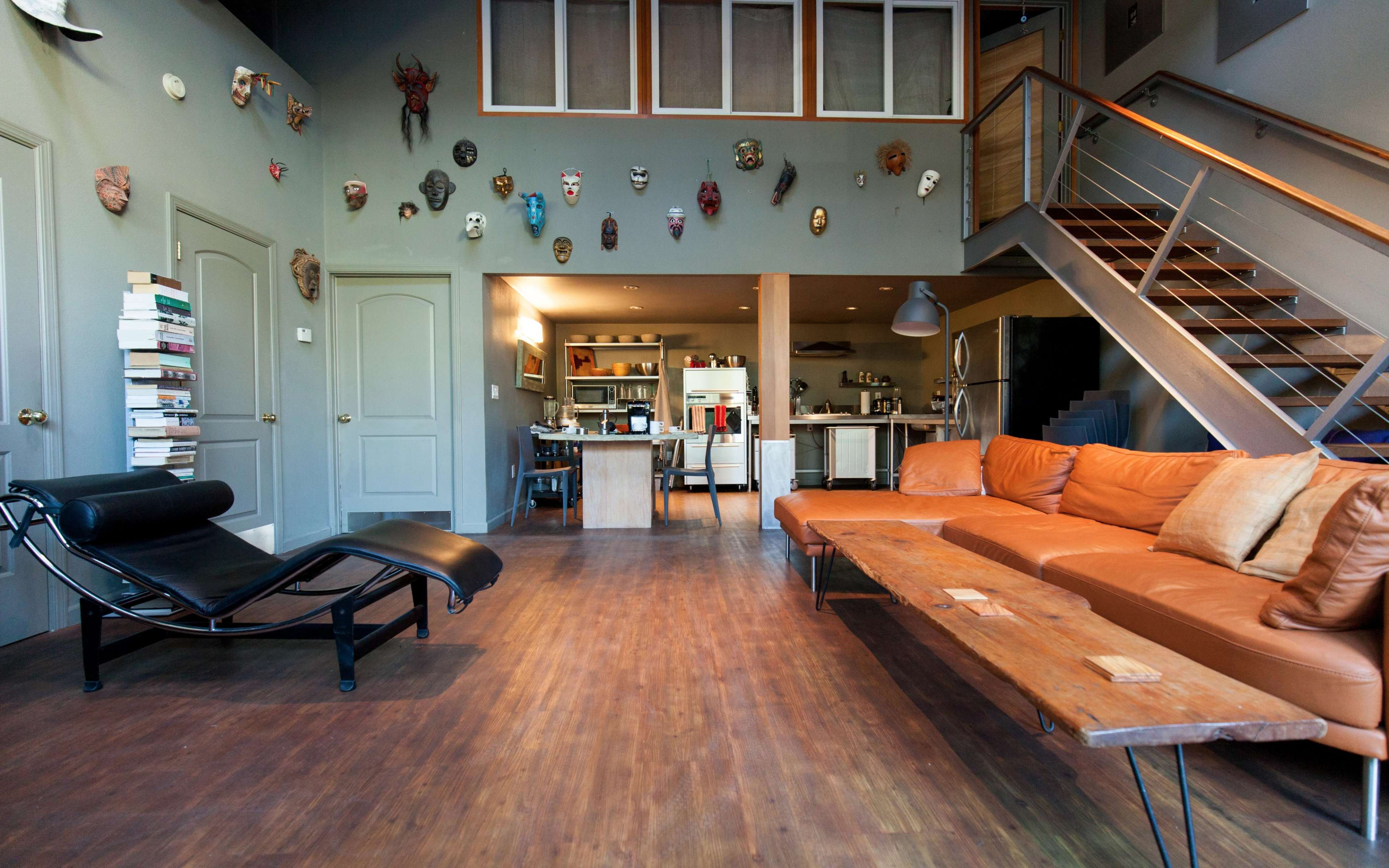 A spacious living area with a leather sofa, a chaise lounge, and a wooden coffee table, featuring eclectic wall decor and an open kitchen in the background.