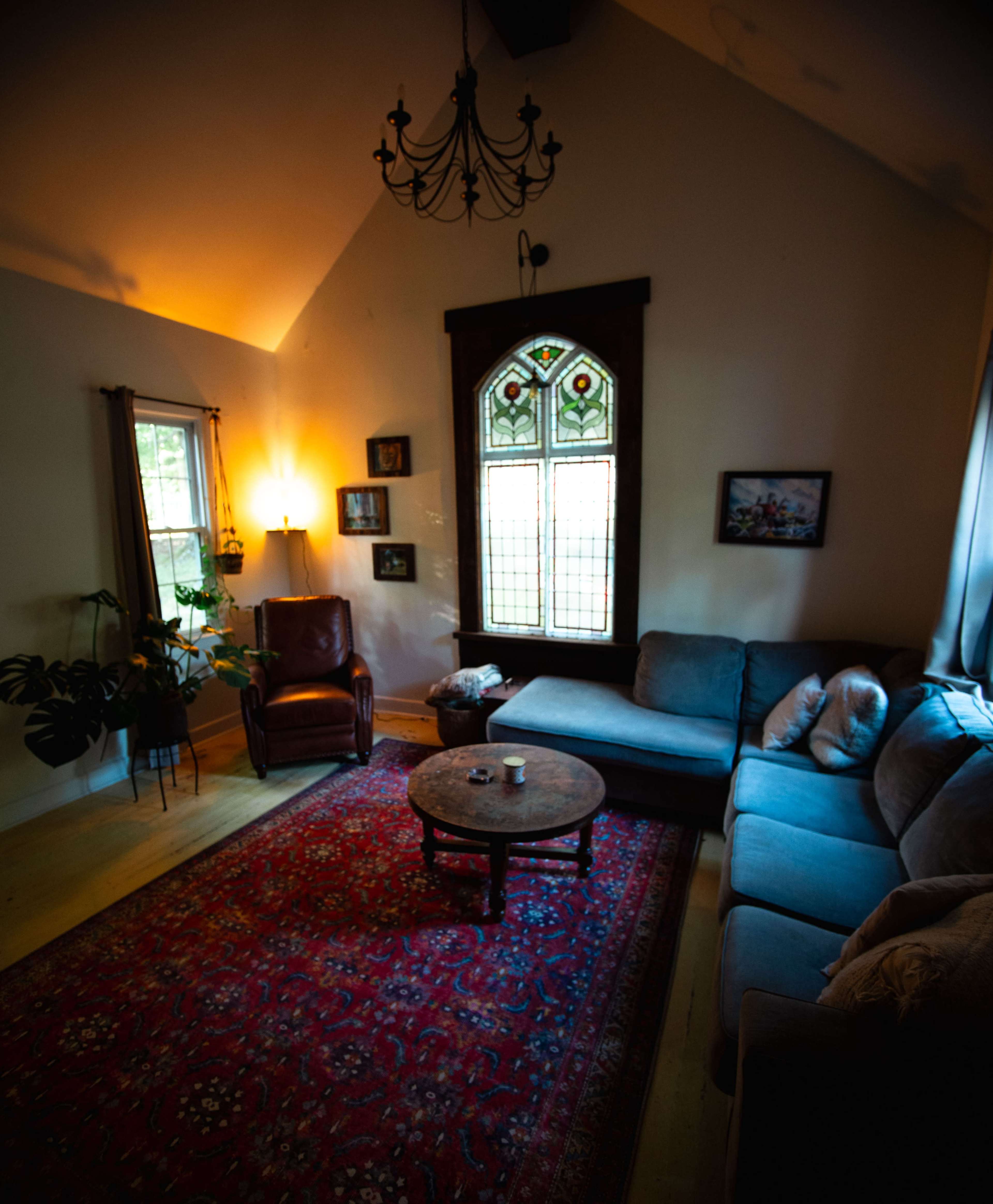 The living room features a comfortable seating area with a sofa and an armchair, a round coffee table, and a stained glass window.