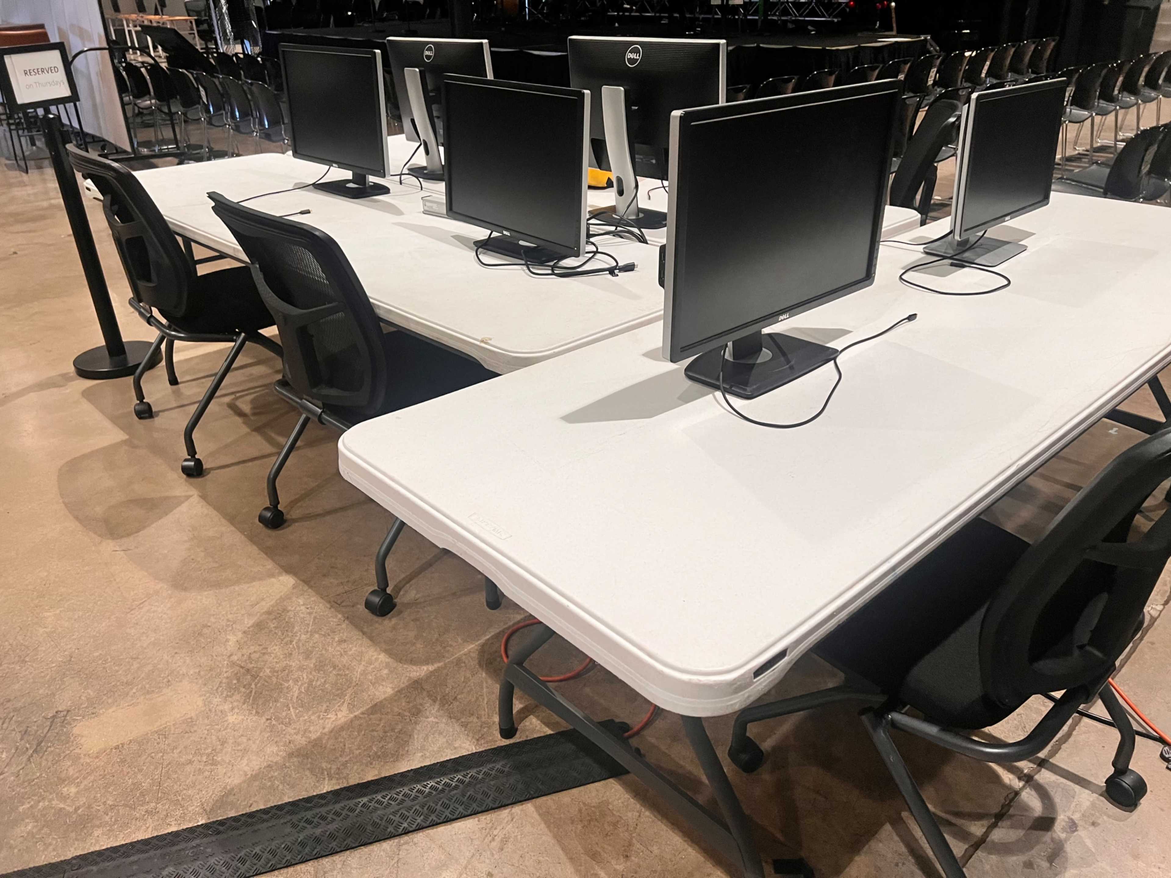 The image shows several black computer monitors arranged on tables in a space set up for an event.