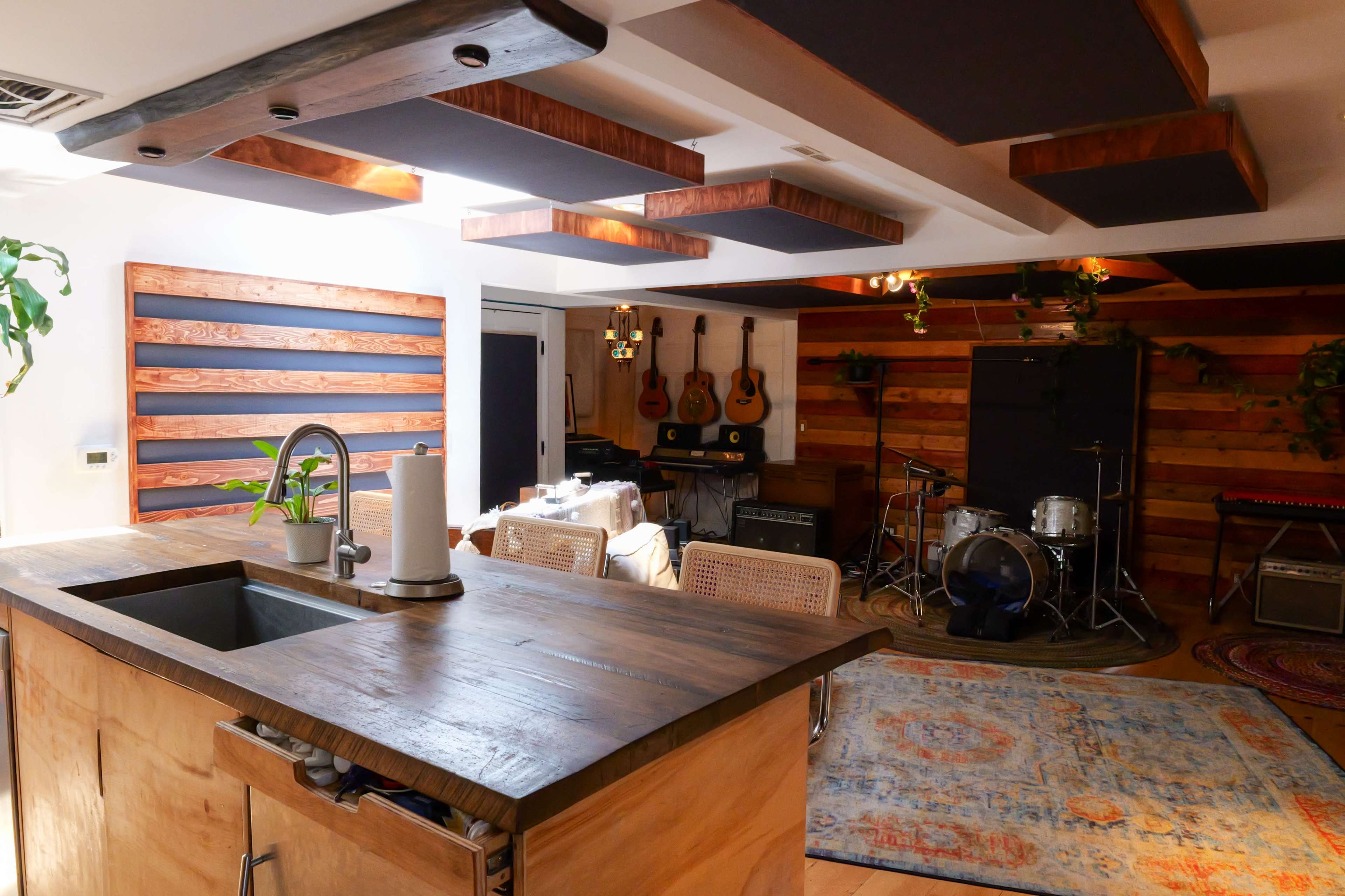 A modern interior featuring a kitchen area with a wooden island, adjacent to a music space with guitars on the wall and a drum set.