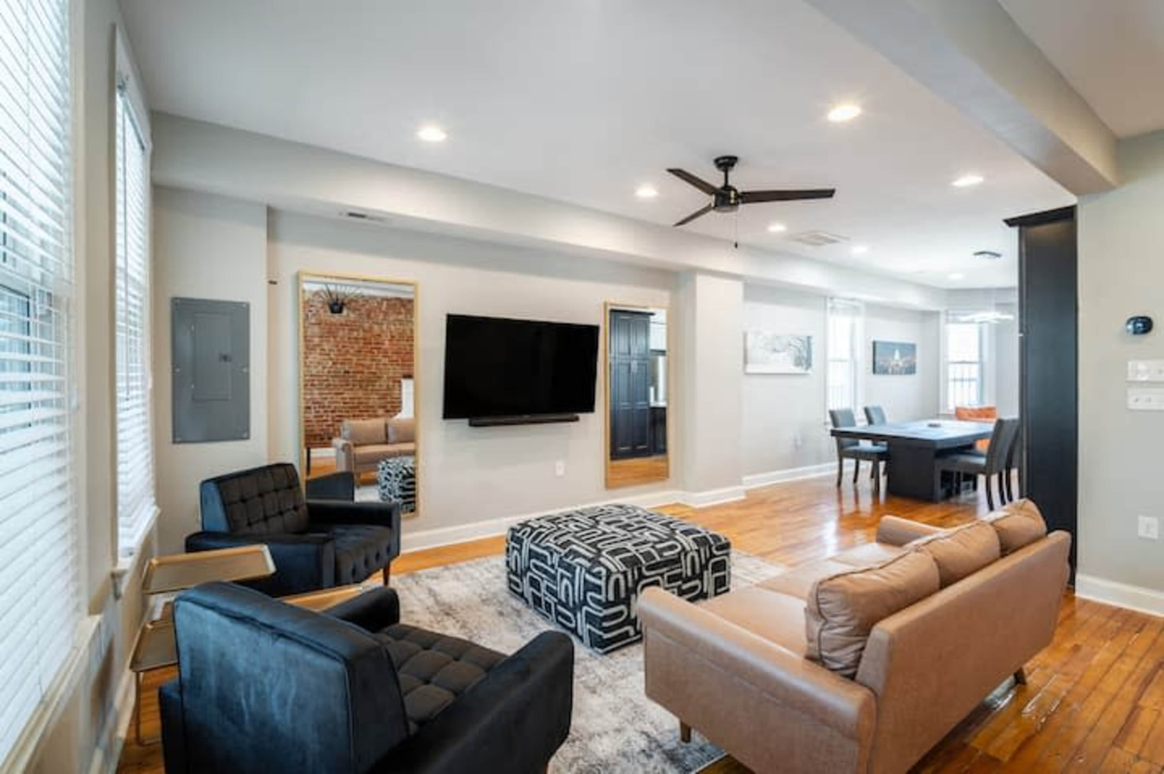 A modern living room features a television mounted on the wall, a seating area with a coffee table, and visible dining space in the background.