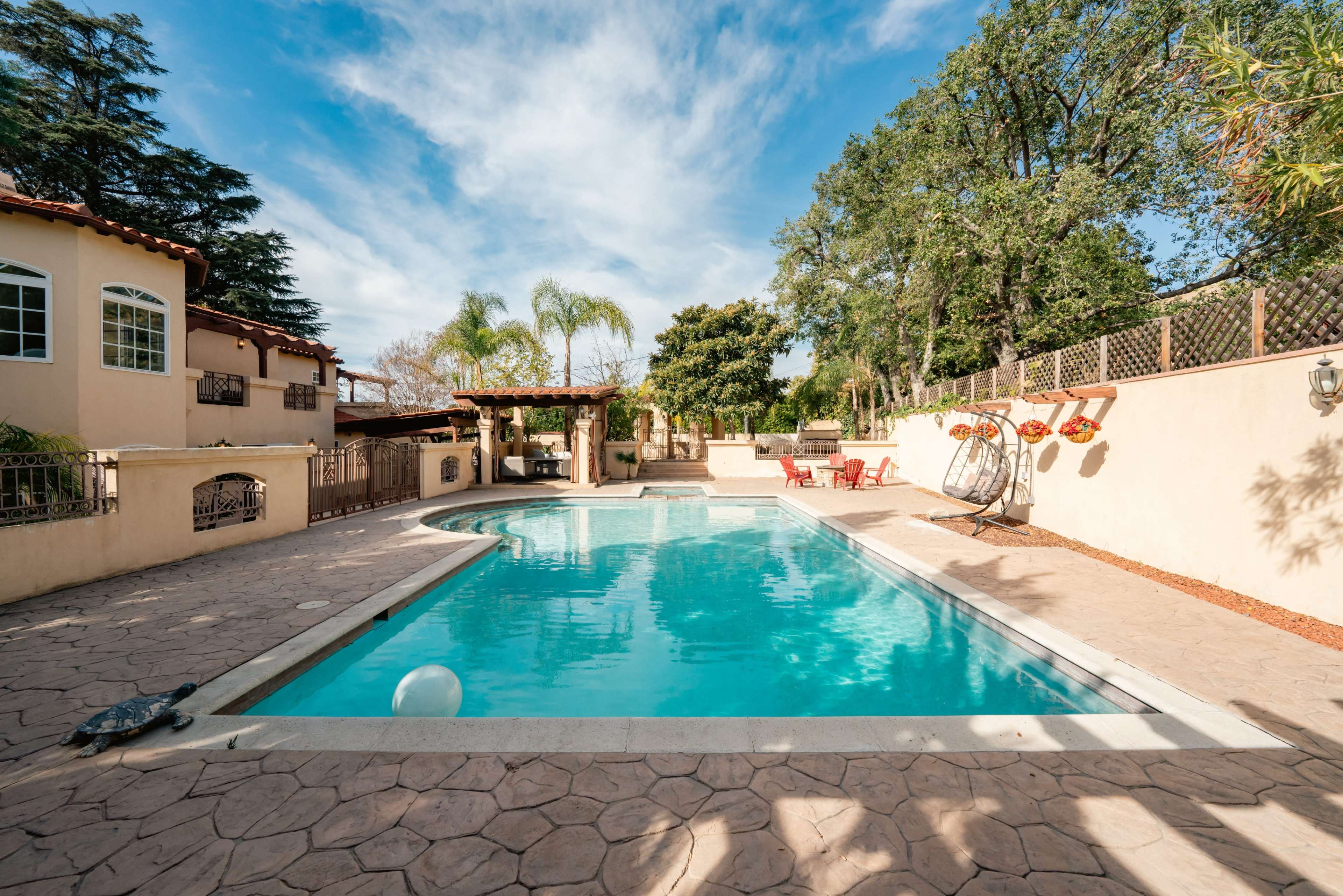 The image shows a swimming pool surrounded by a concrete deck, with lounge chairs and trees in the background.