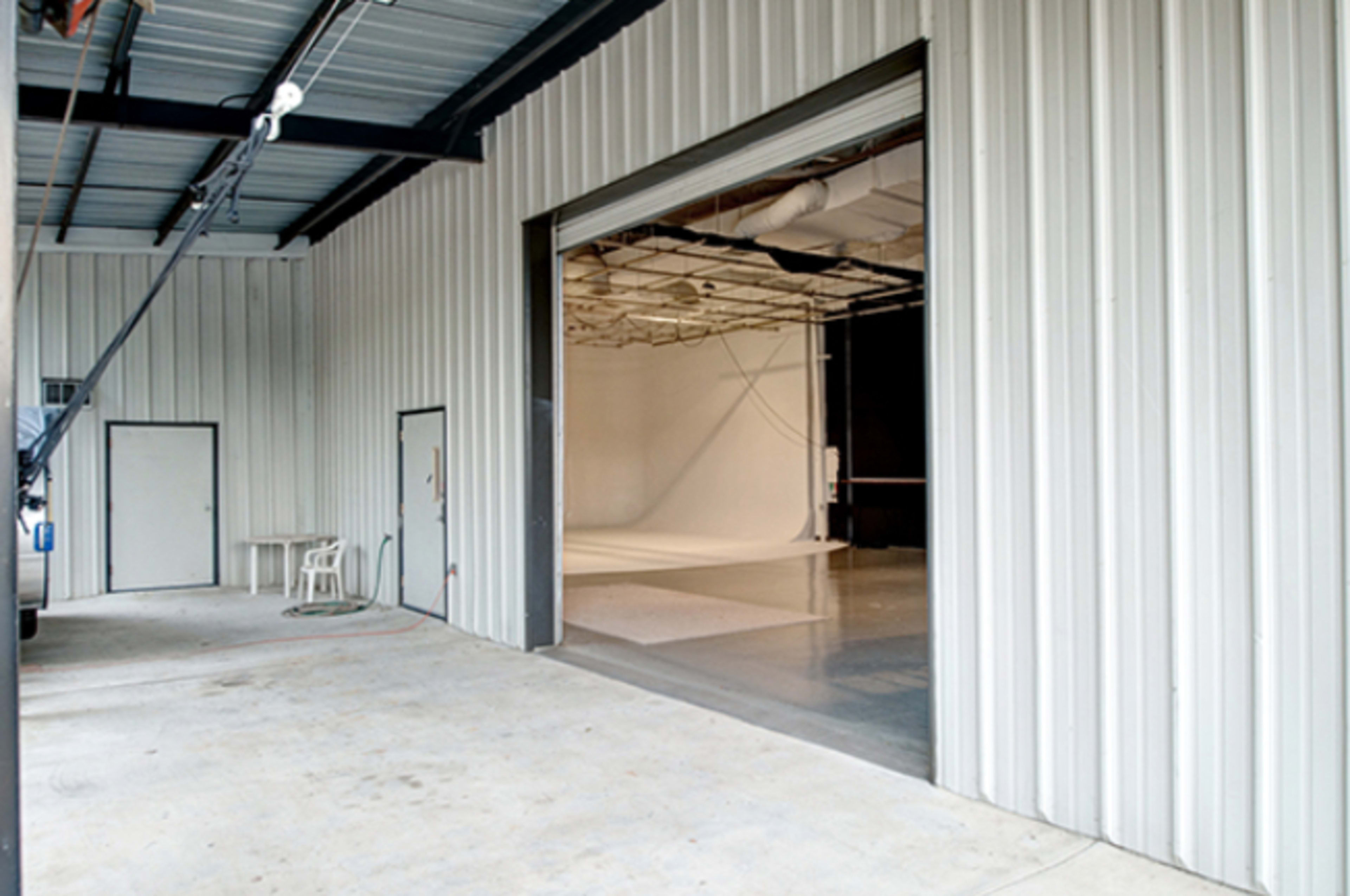 An open industrial garage door leading into a spacious, empty studio area with a white backdrop.