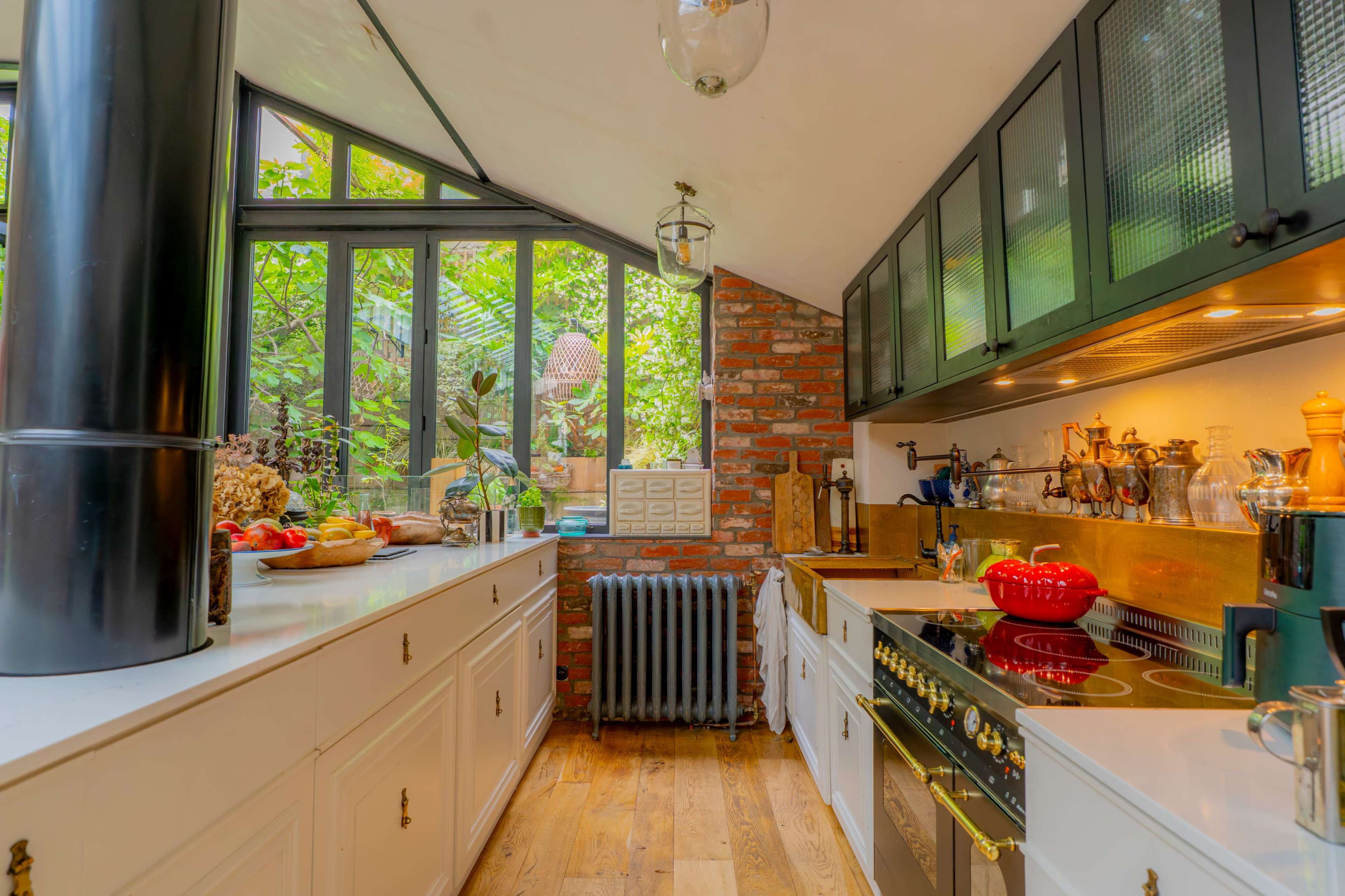 The kitchen features modern appliances, white cabinetry, exposed brick walls, and large windows that allow natural light to illuminate the space.
