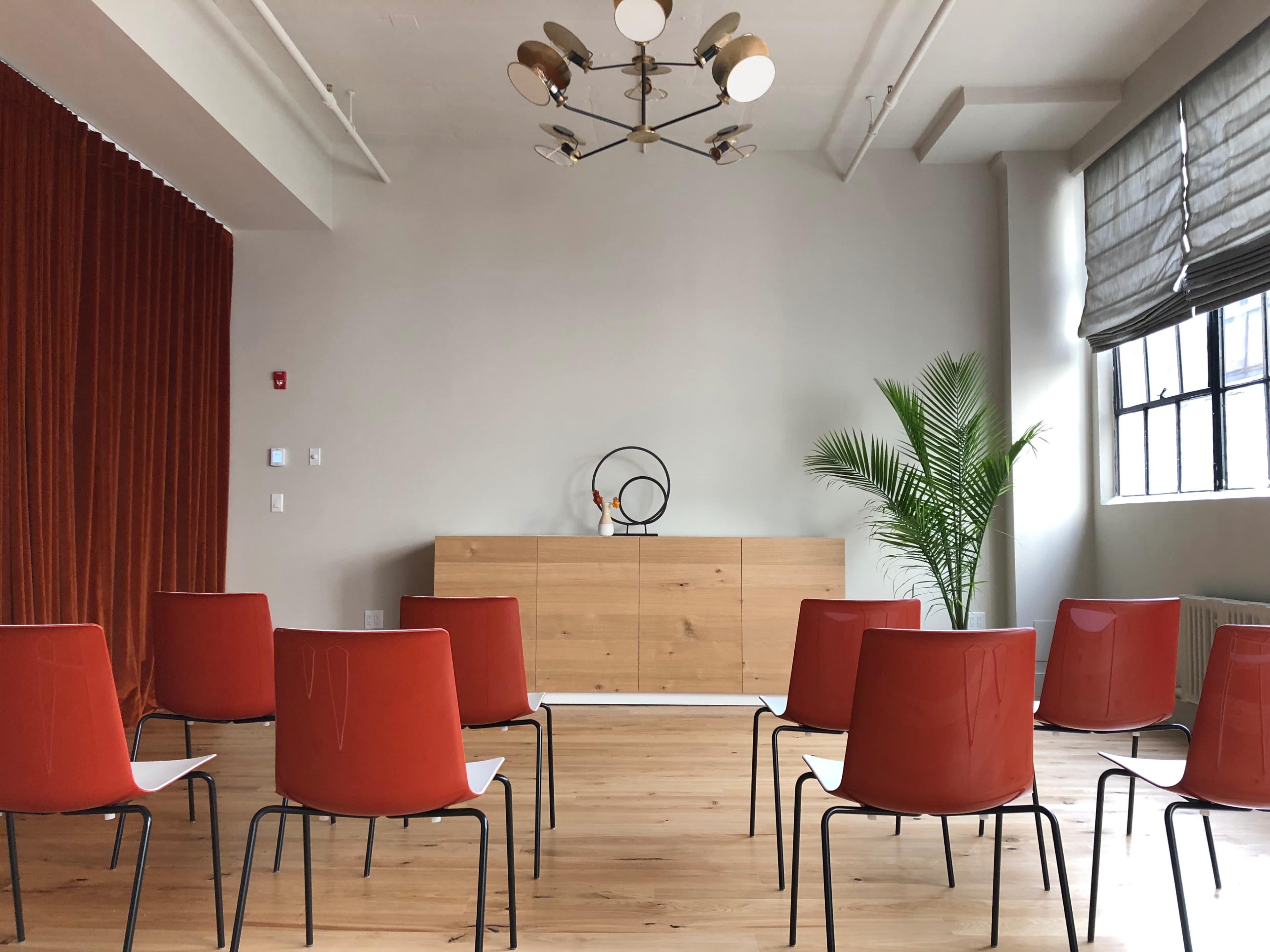 A minimalist meeting room with red chairs arranged neatly in a circle, a wooden cabinet against the wall, and a potted plant in the corner.