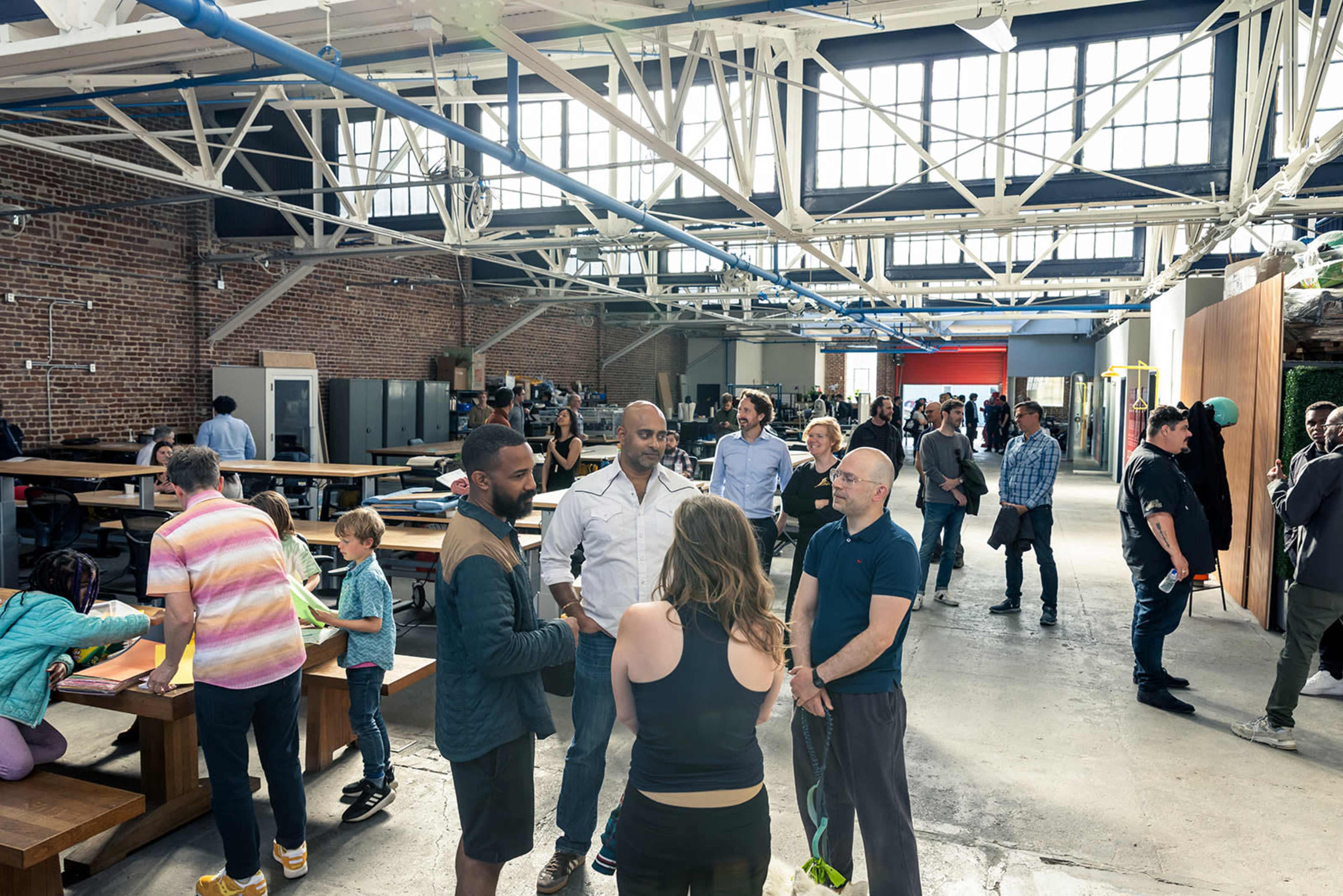 A diverse group of people mingles in a large, industrial-style venue with exposed brick walls and high ceilings.