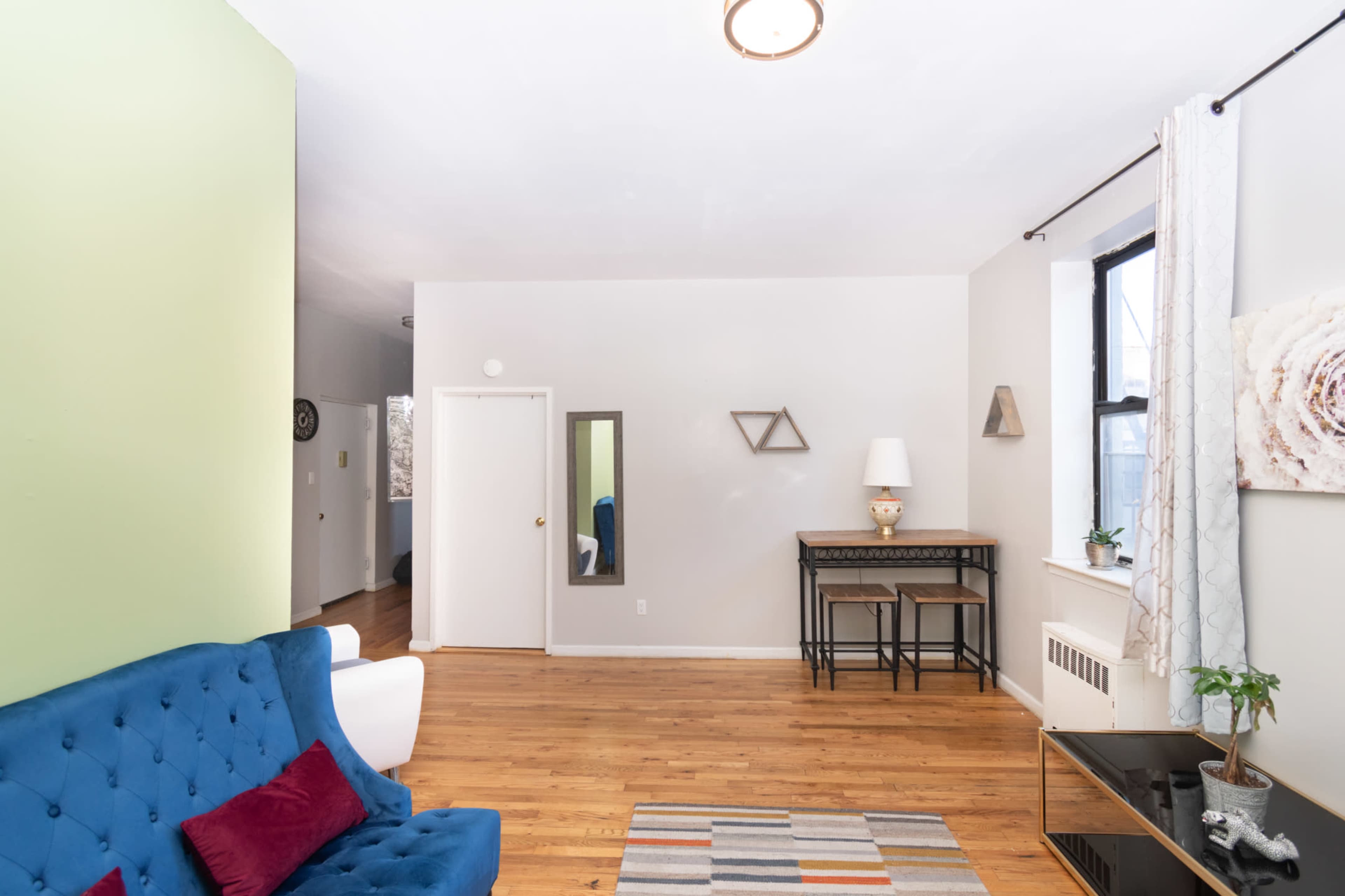 The living room features a blue sofa, a mirror, a small table with chairs, and wooden flooring, with green and gray walls.
