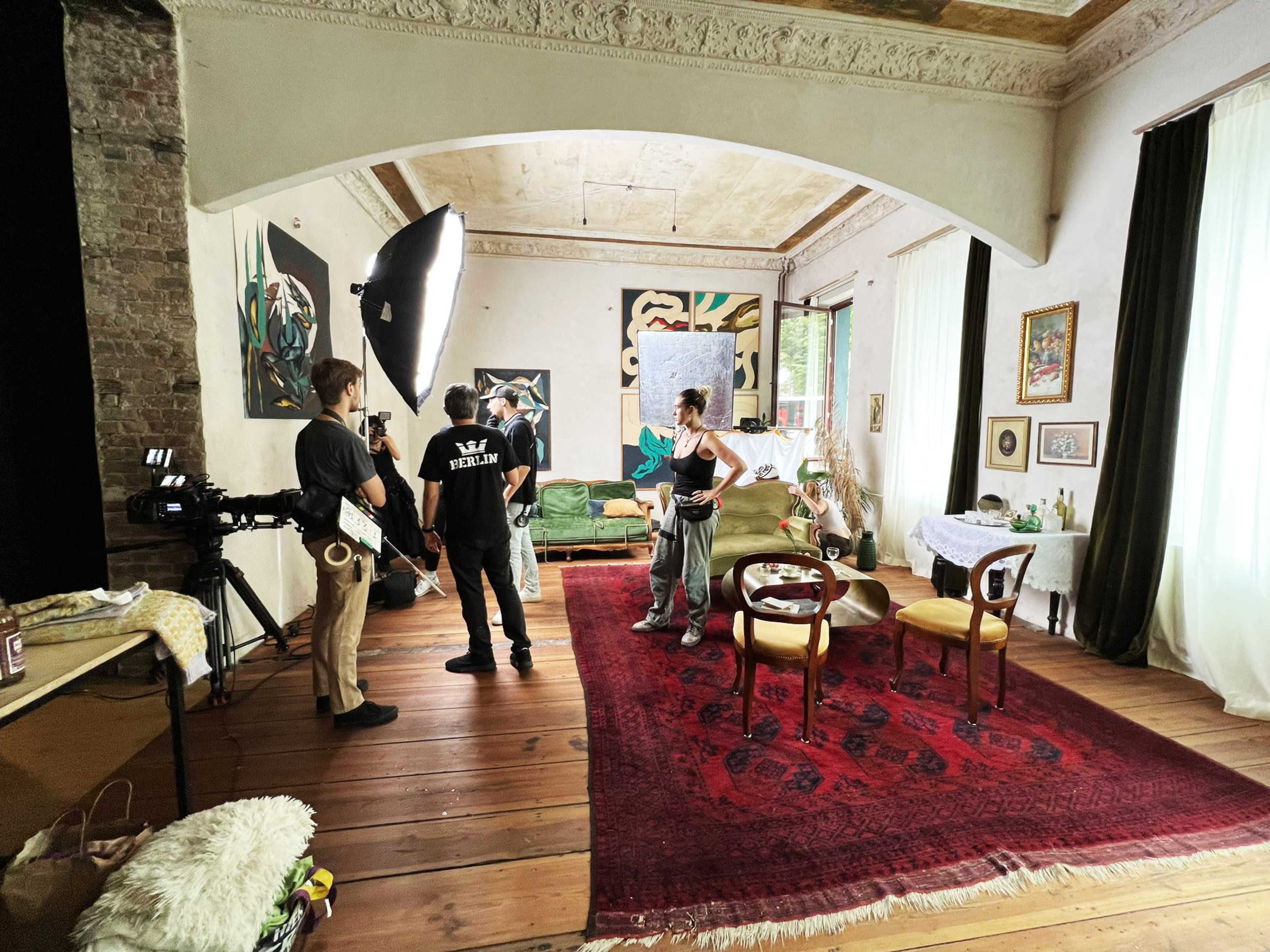 A film crew sets up in a spacious room featuring vintage furniture and artwork on the walls.
