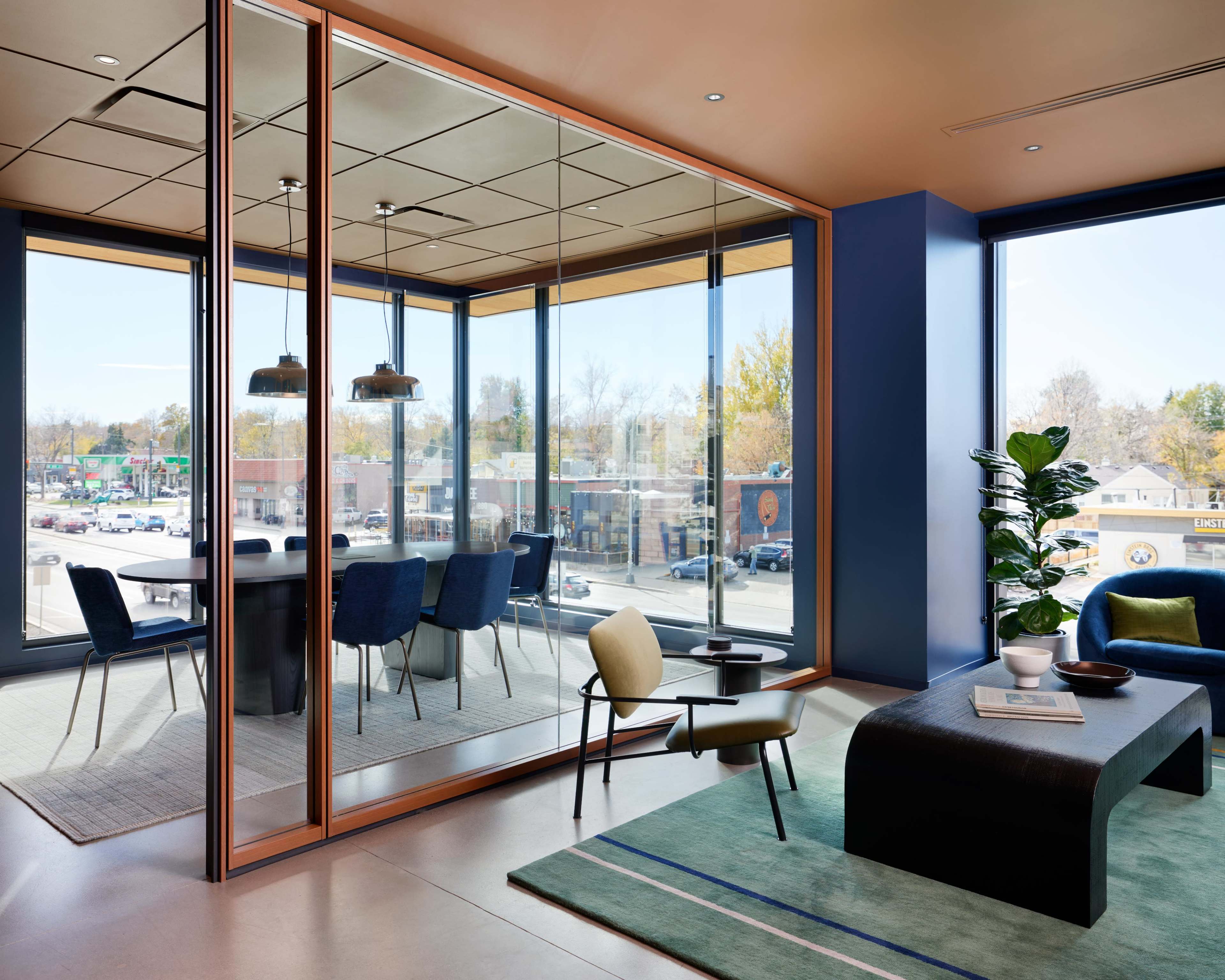 A modern office interior with a glass-walled meeting room, a seating area, and a view of an outdoor parking lot.