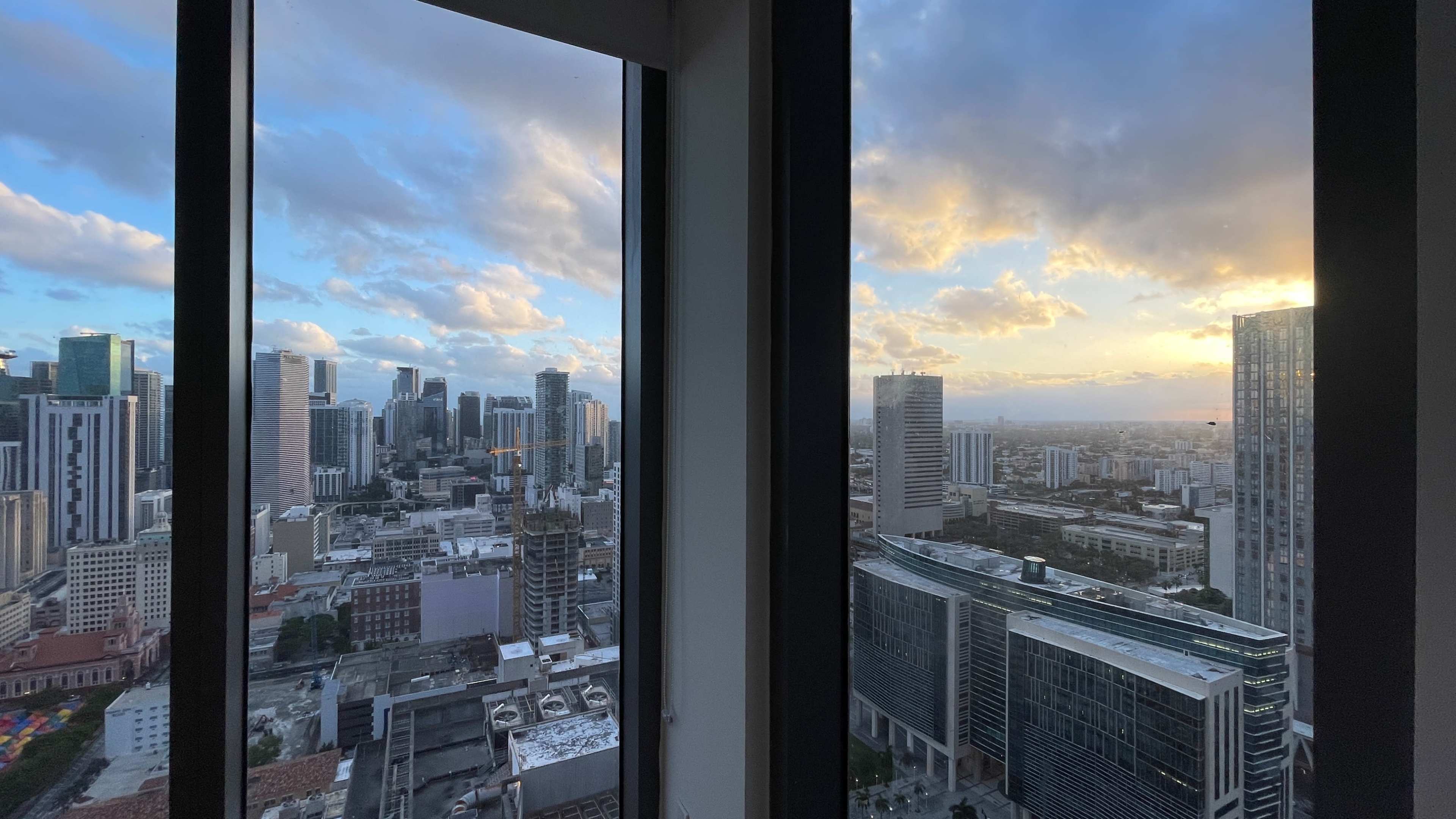 A cityscape view from a high-rise building, featuring skyscrapers and a sunset in the background.
