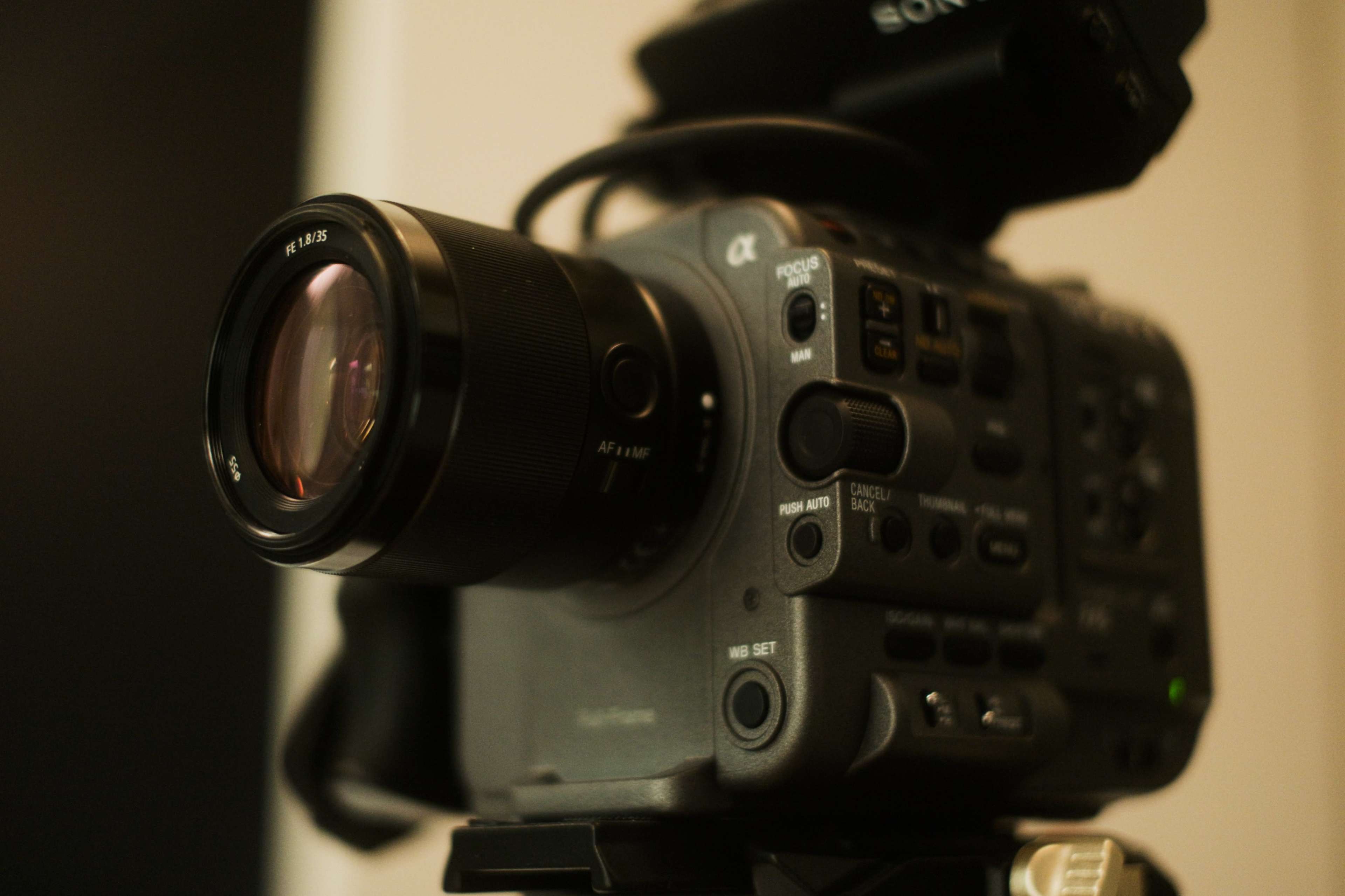 A close-up view of a professional camera with various control buttons and a lens attached, positioned on a tripod.