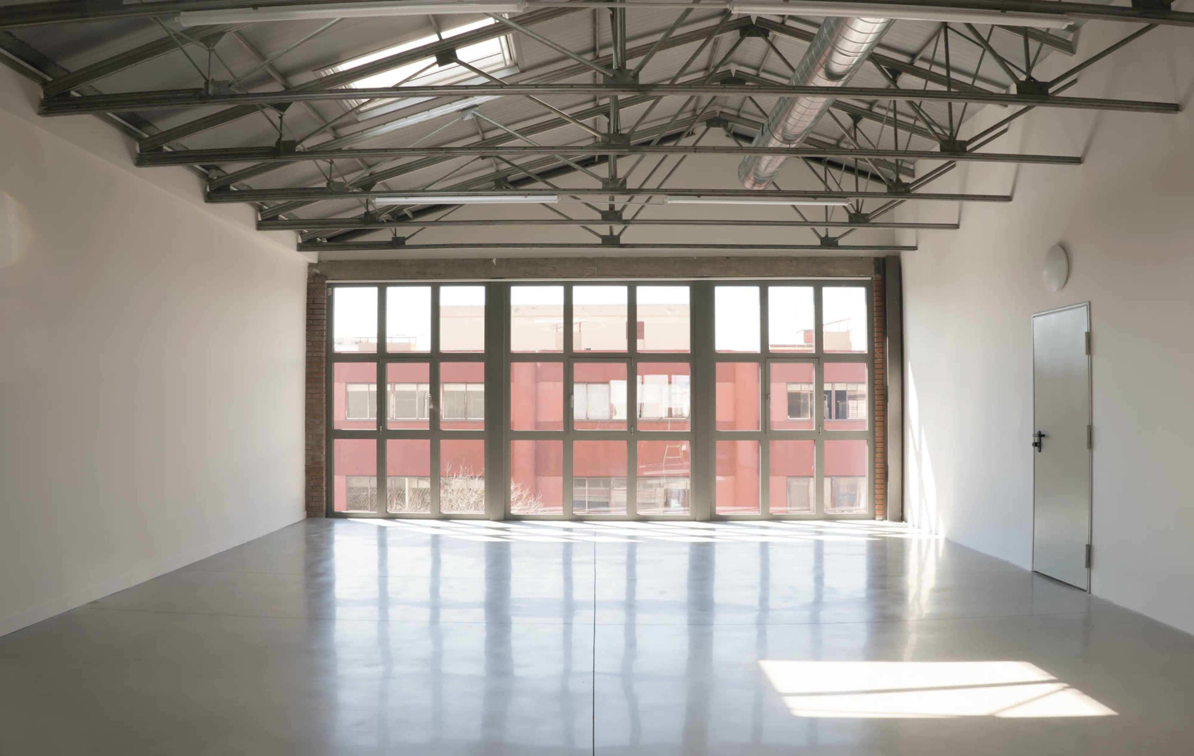 An empty room with large windows, high ceilings, and polished concrete flooring.