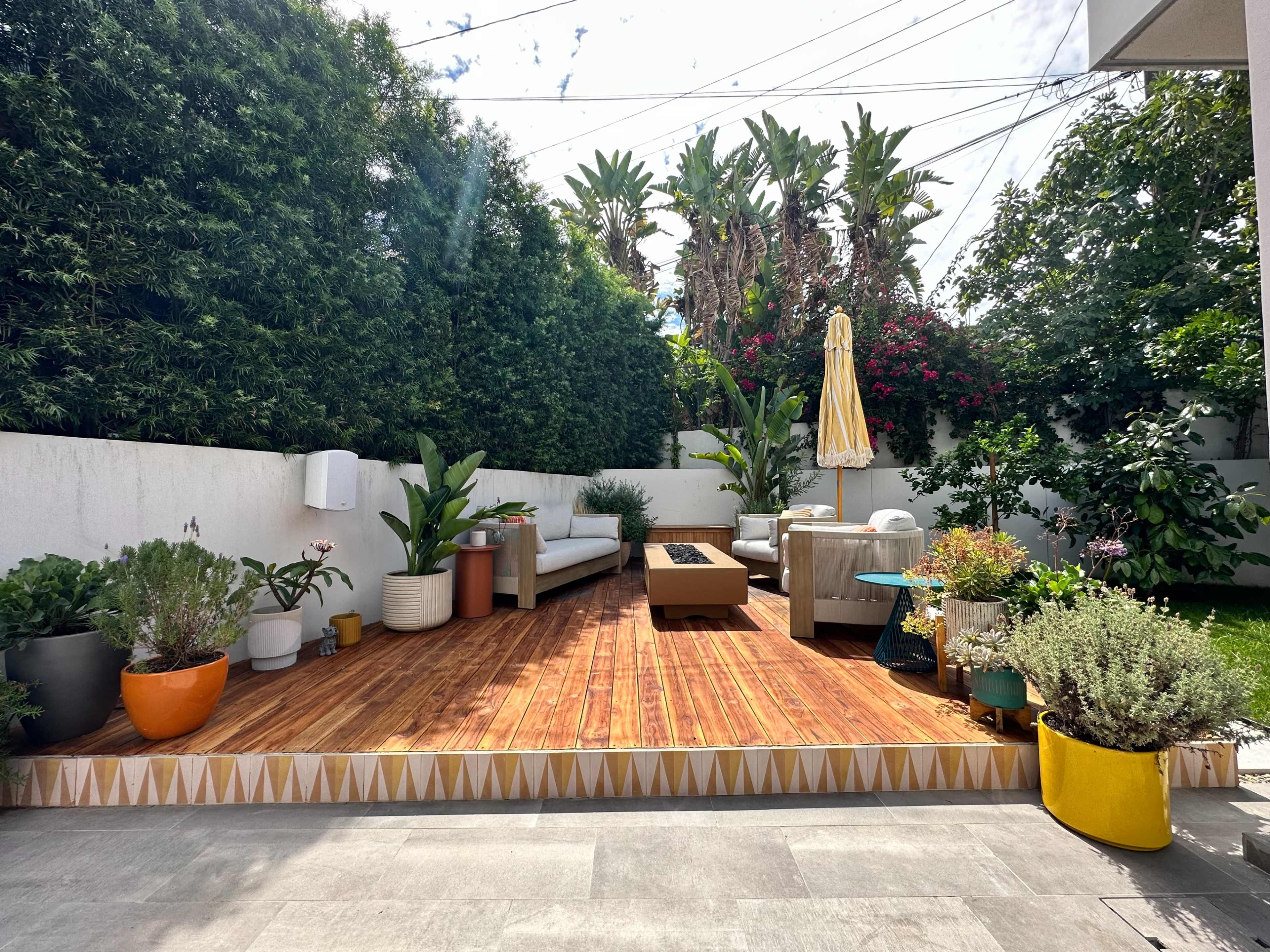 A wooden deck surrounded by various potted plants and outdoor furniture in a garden setting.