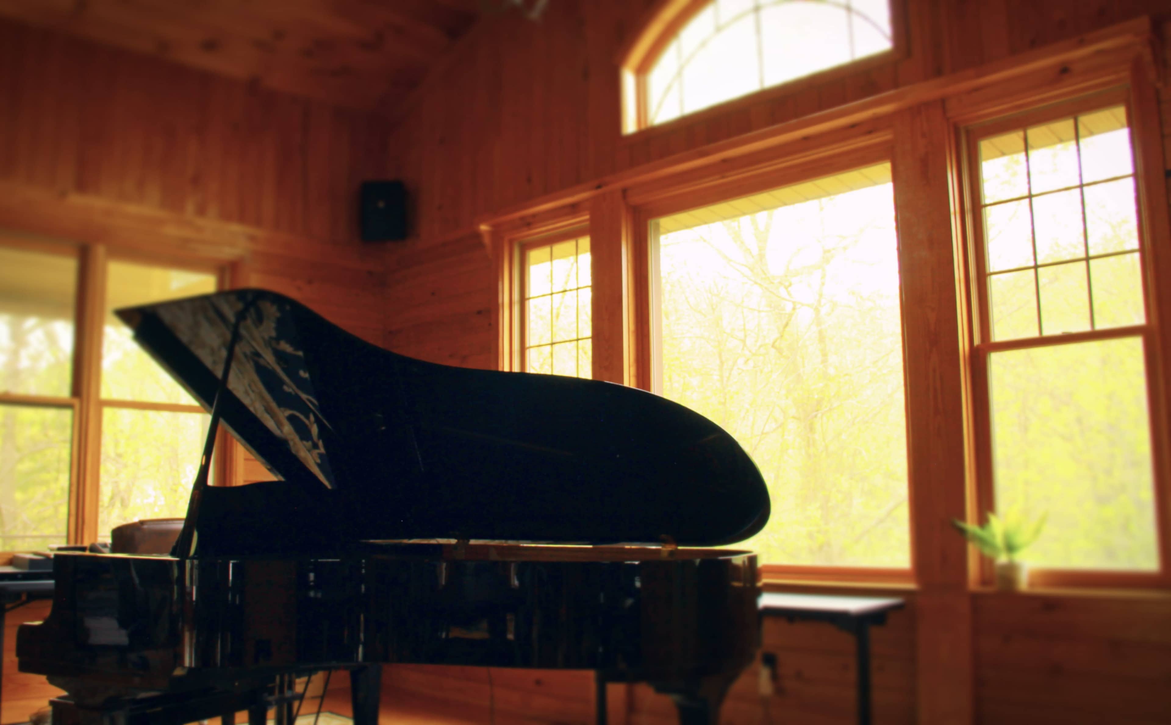 A grand piano sits in a wooden room with large windows letting in natural light.