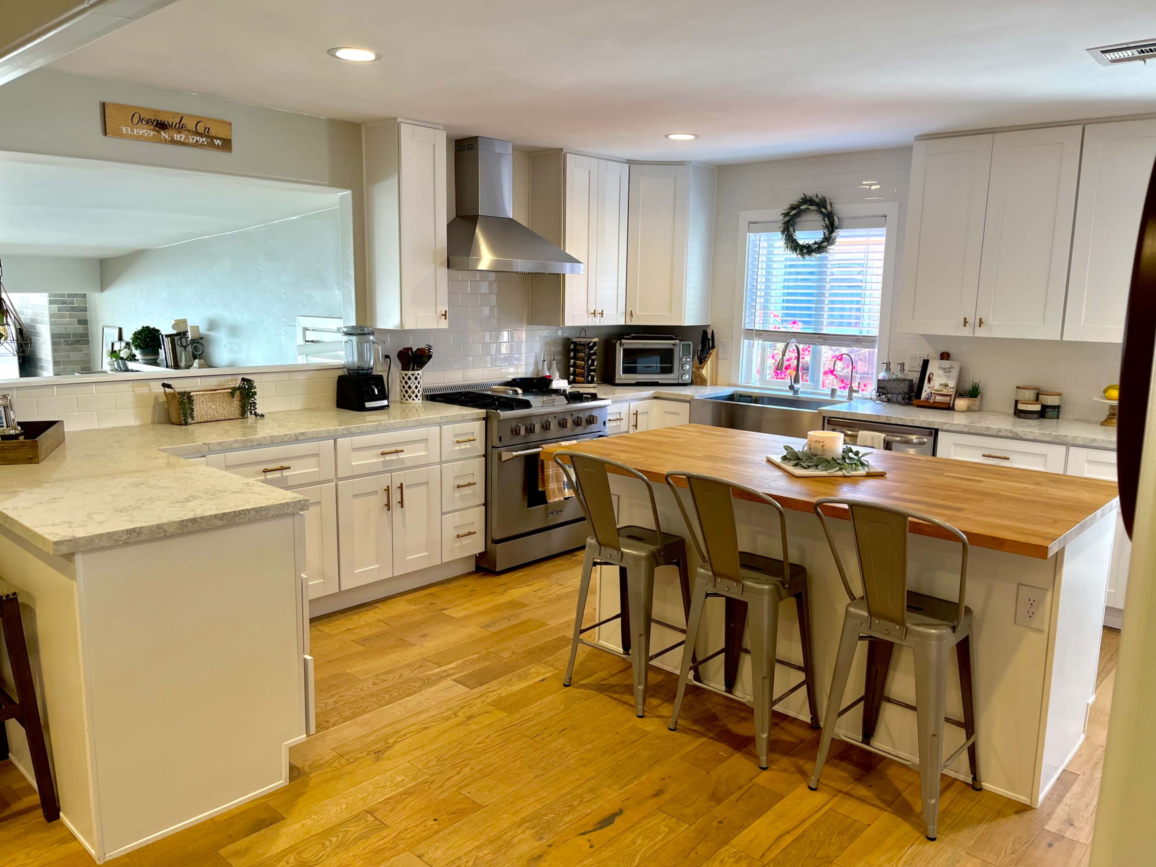 The kitchen features white cabinets, a wooden island with metal stools, and modern appliances.