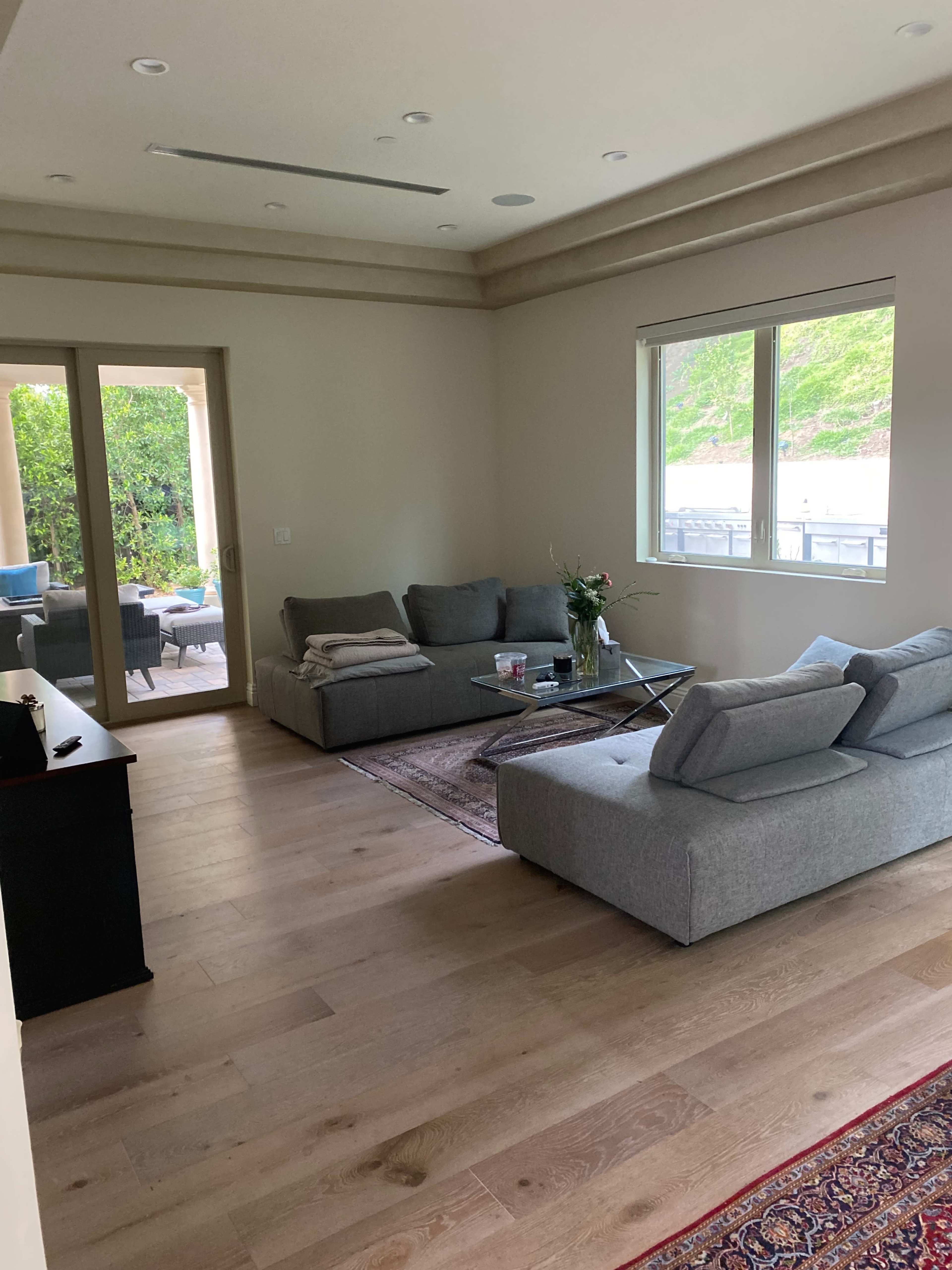 A furnished living room with a gray sectional sofa, a coffee table, and a view of an outdoor area through a set of glass doors.