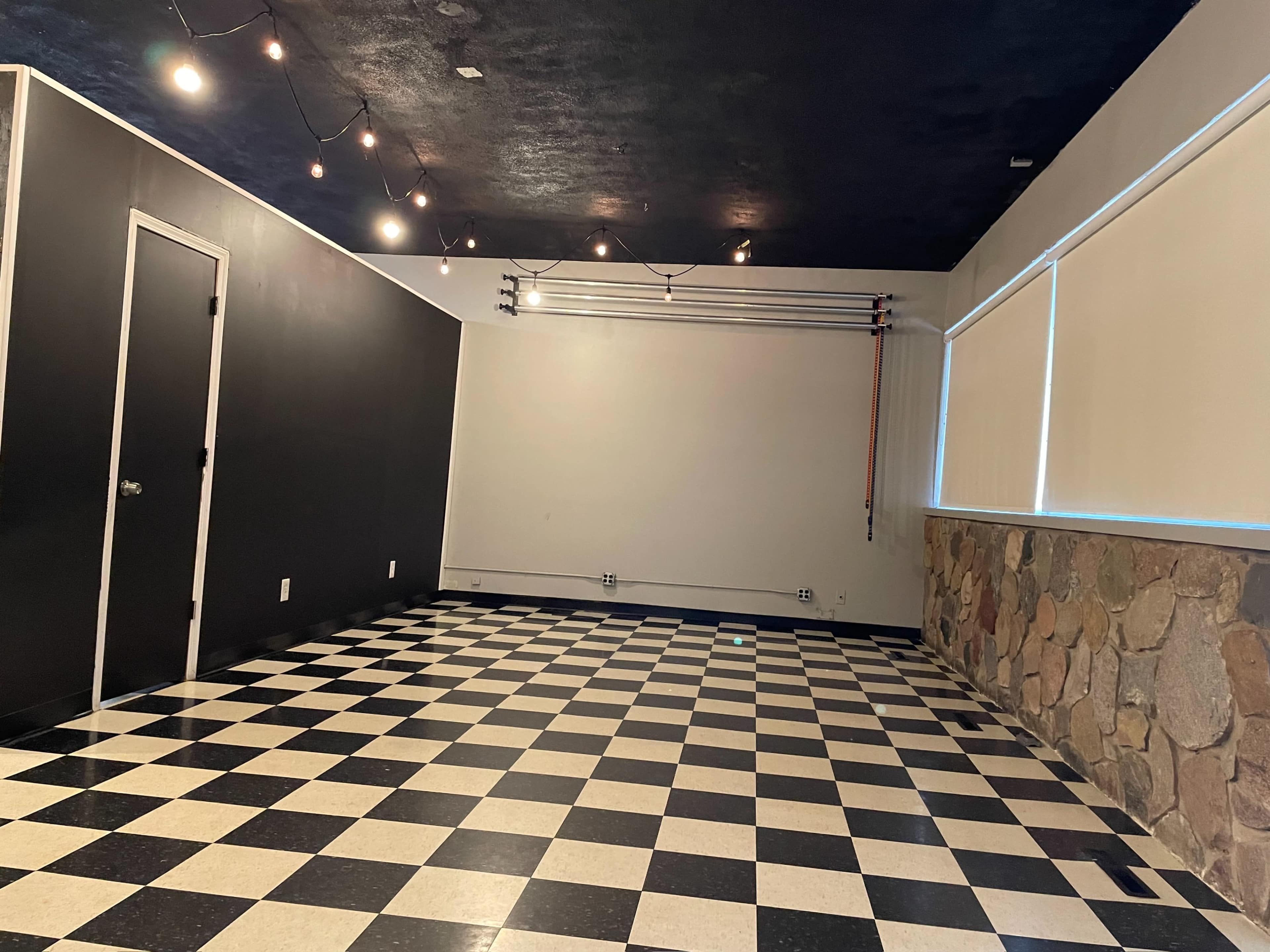 The room features a checkered black and white floor, a stone wall, and overhead string lights illuminating the space.
