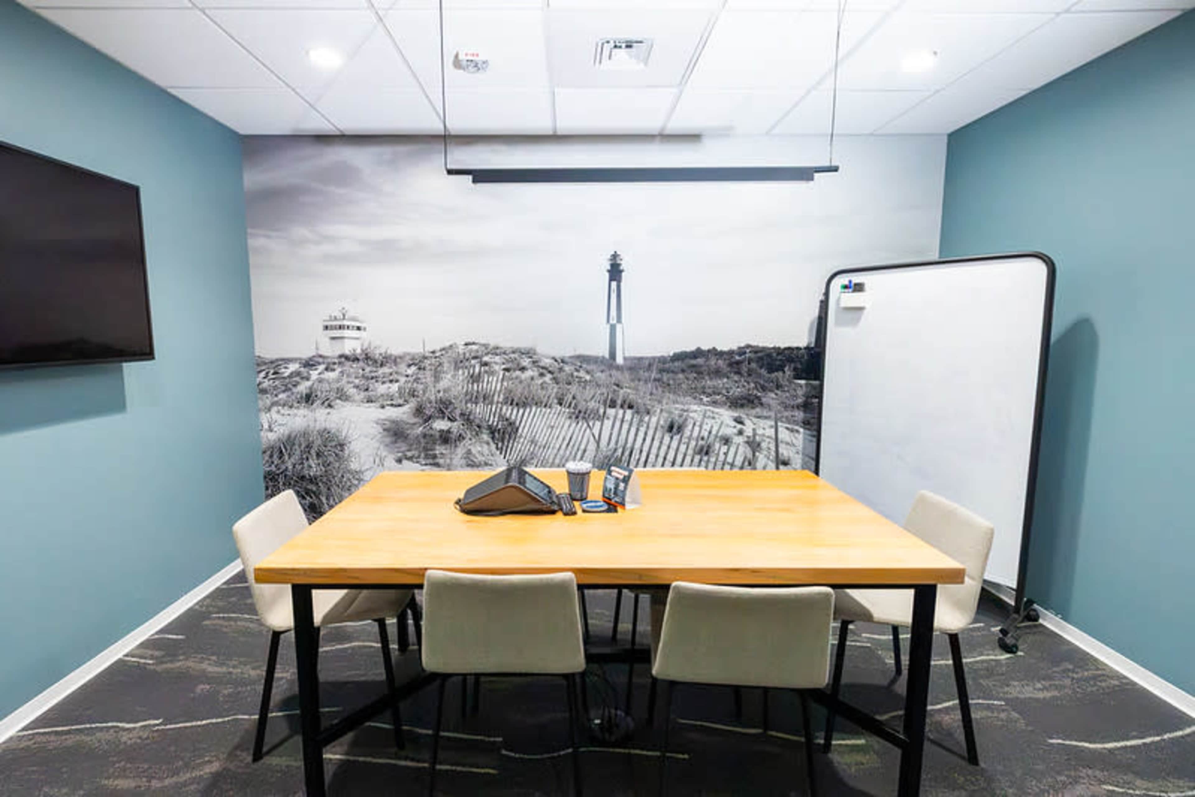 The image shows a modern conference room with a wooden table, four chairs, a television on the wall, and a large mural of a coastal scene featuring a lighthouse.
