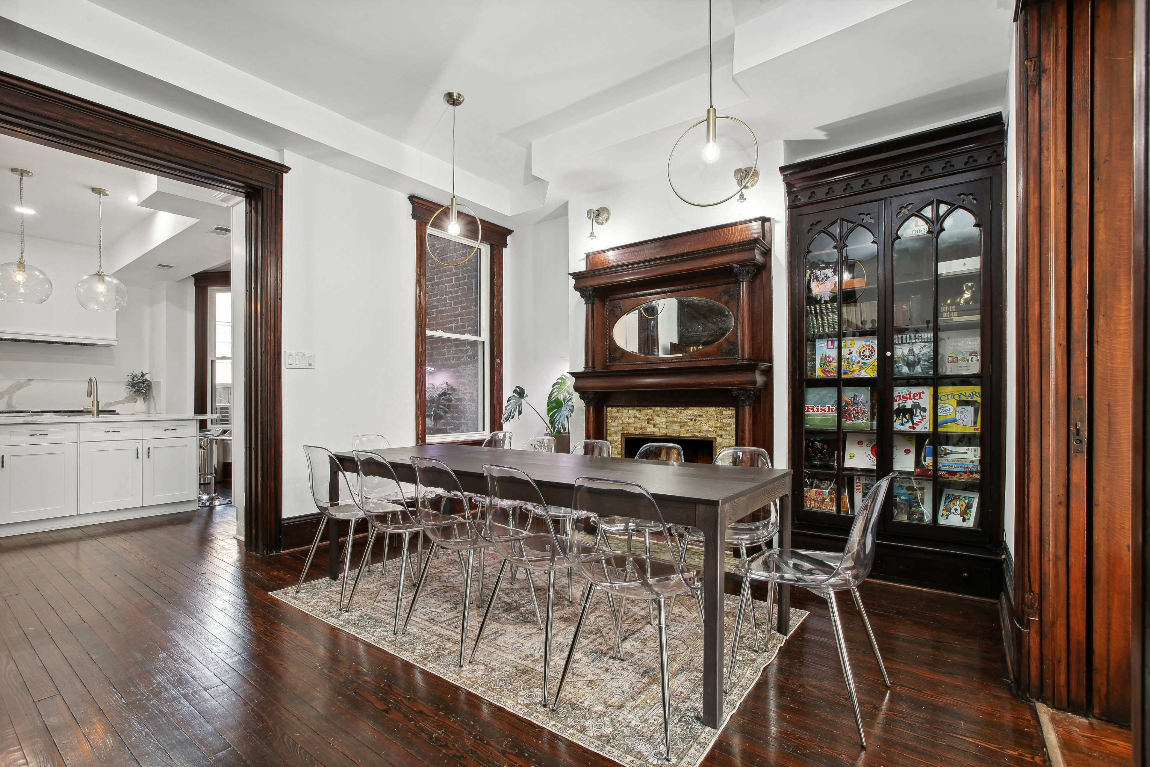 The image shows a spacious dining area featuring a long table with clear chairs, a decorative fireplace, and built-in shelving units displaying colorful items.