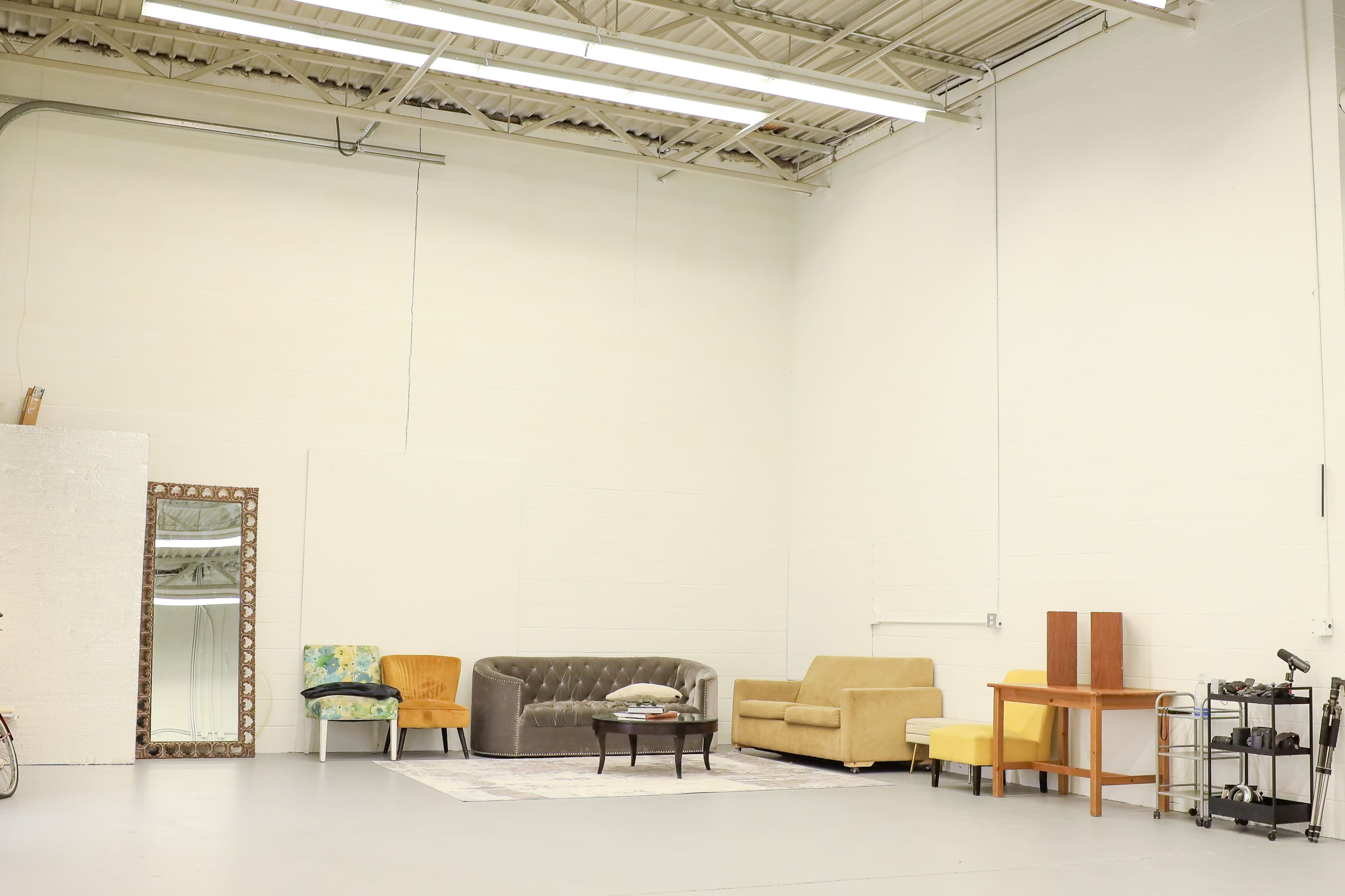 A spacious room with a light-colored floor, featuring a variety of seating options, a mirror, and a small table against the wall.