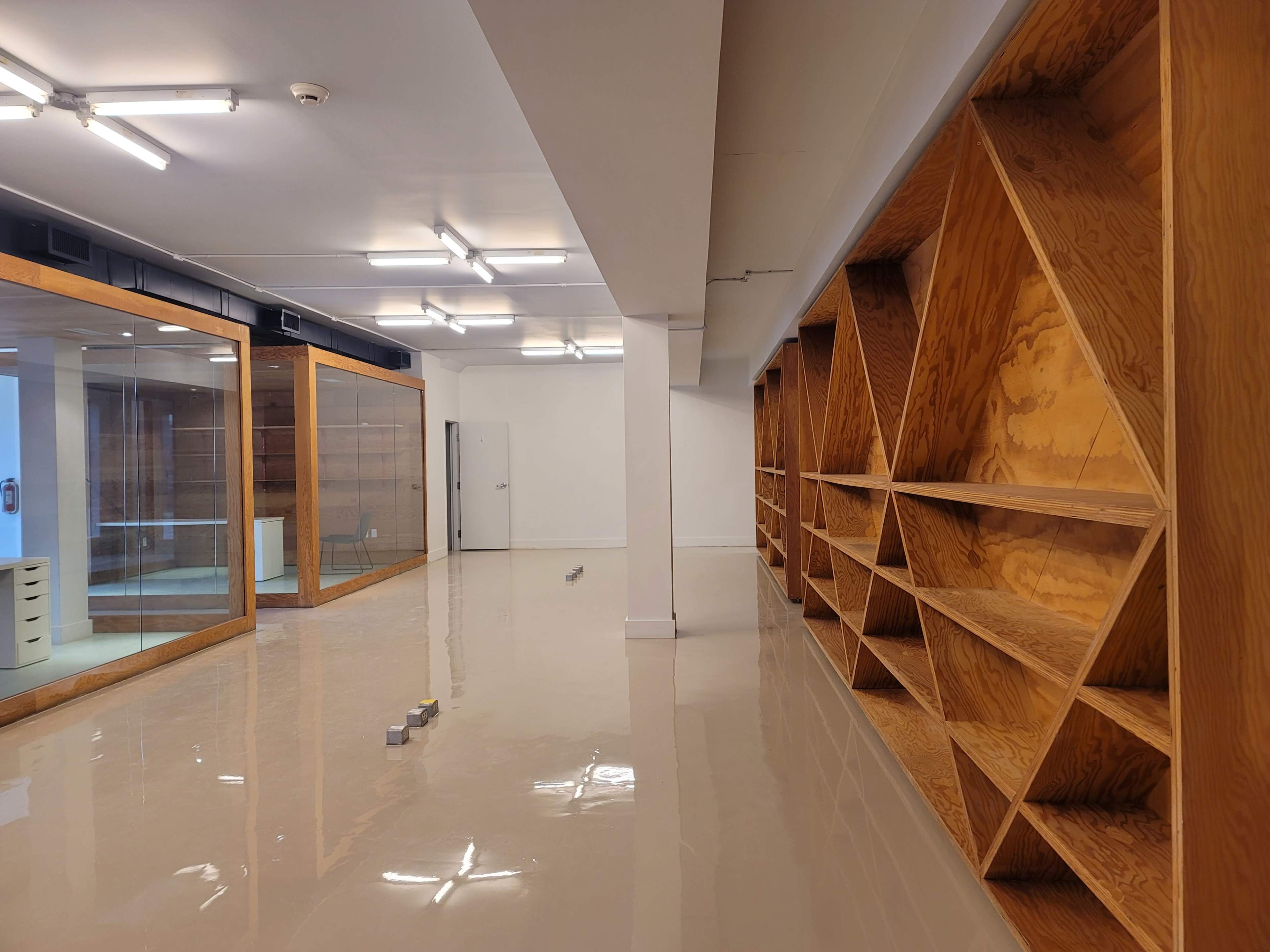 A spacious interior room with polished floors, wooden shelving units along one wall, and glass partitions separating additional areas.