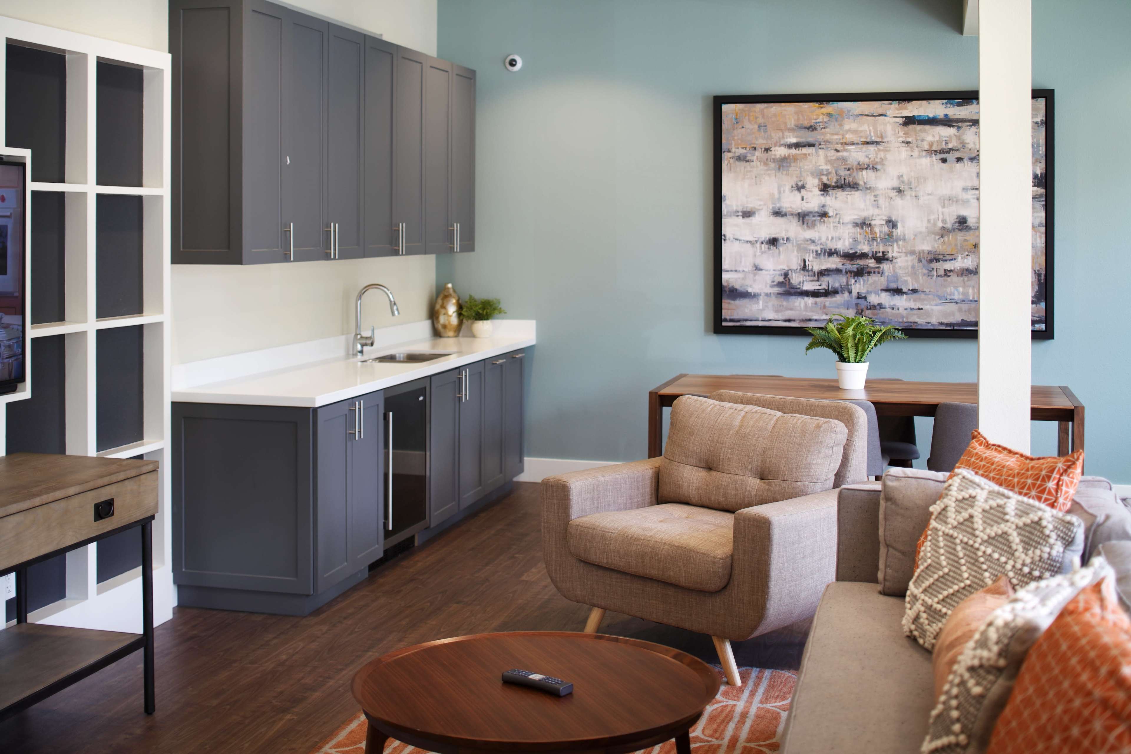 A modern living space featuring a gray kitchen cabinet area, a cozy seating arrangement, and a table with a decorative painting on the wall.