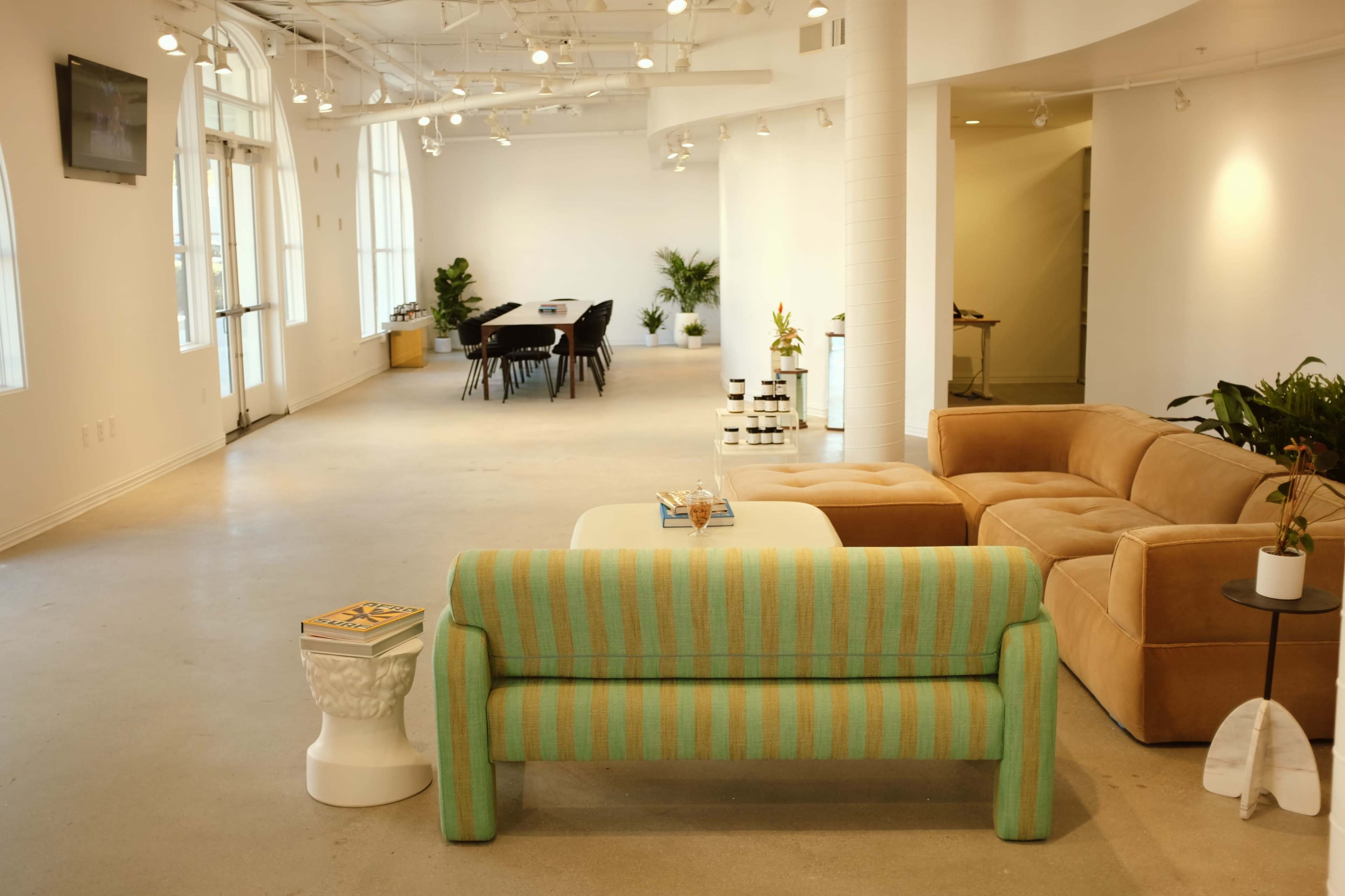 A spacious, modern office interior with a striped couch, a coffee table, and a dining area in the background featuring a long table and chairs.