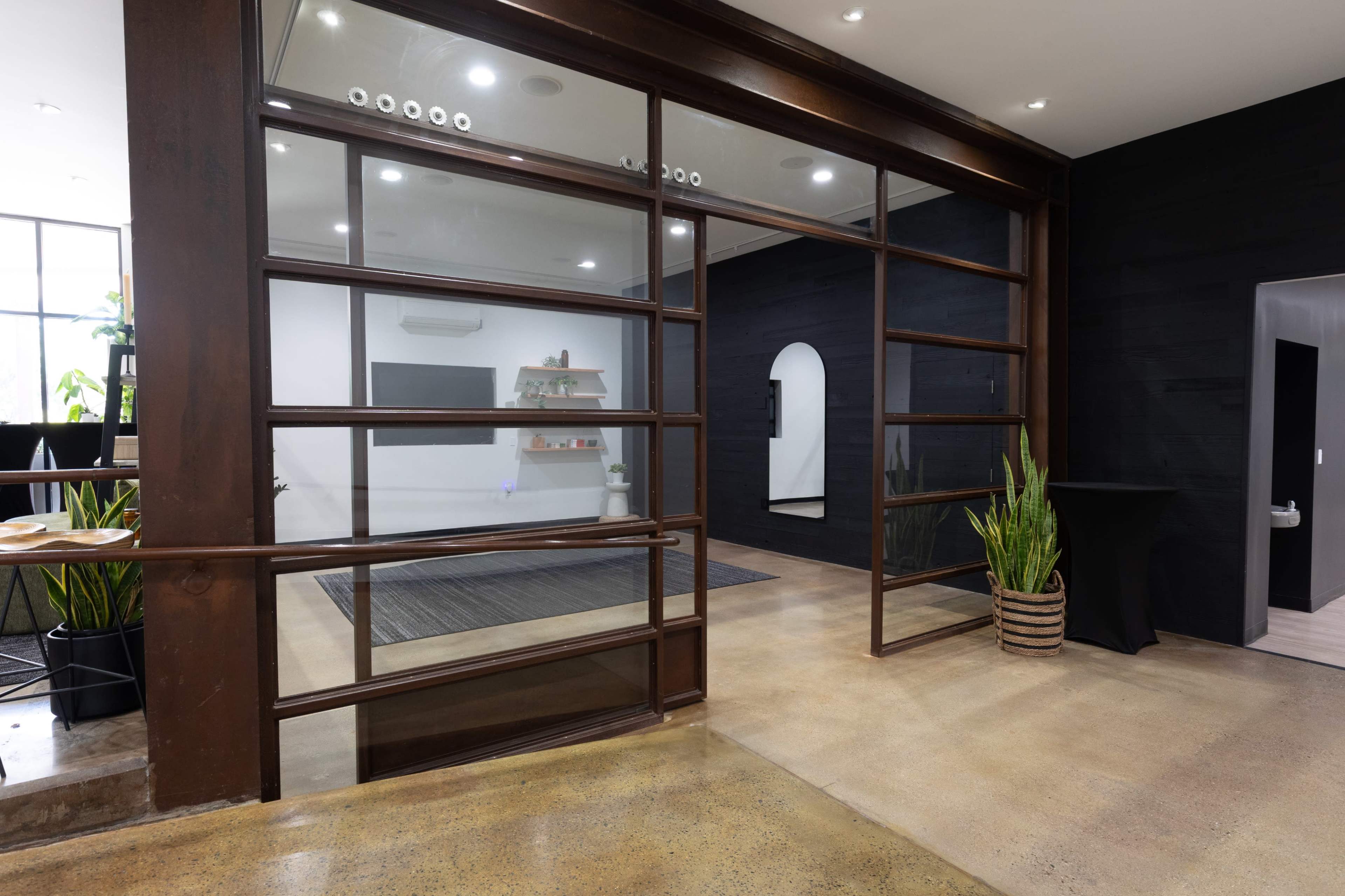 The image shows a modern interior space with glass walls separating rooms, featuring polished concrete floors and minimalist decor.
